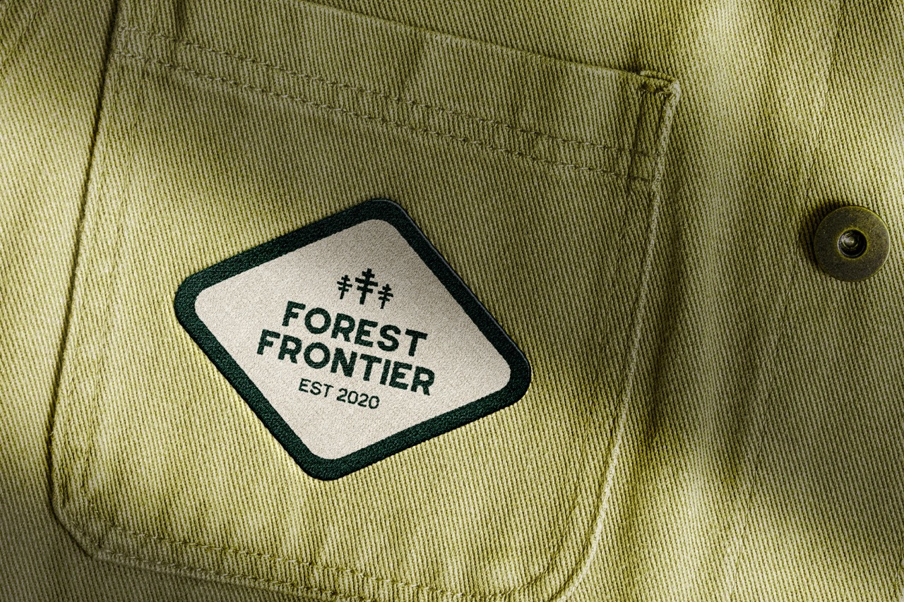 White embroidered logo reading 'forest frontier' on the pocket of green-khaki clothing.
