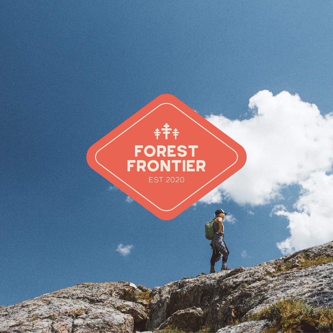 Film-style photo of a person hiking on a tor with a blue sky, red sticker that reads 'forest frontier' in the centre.