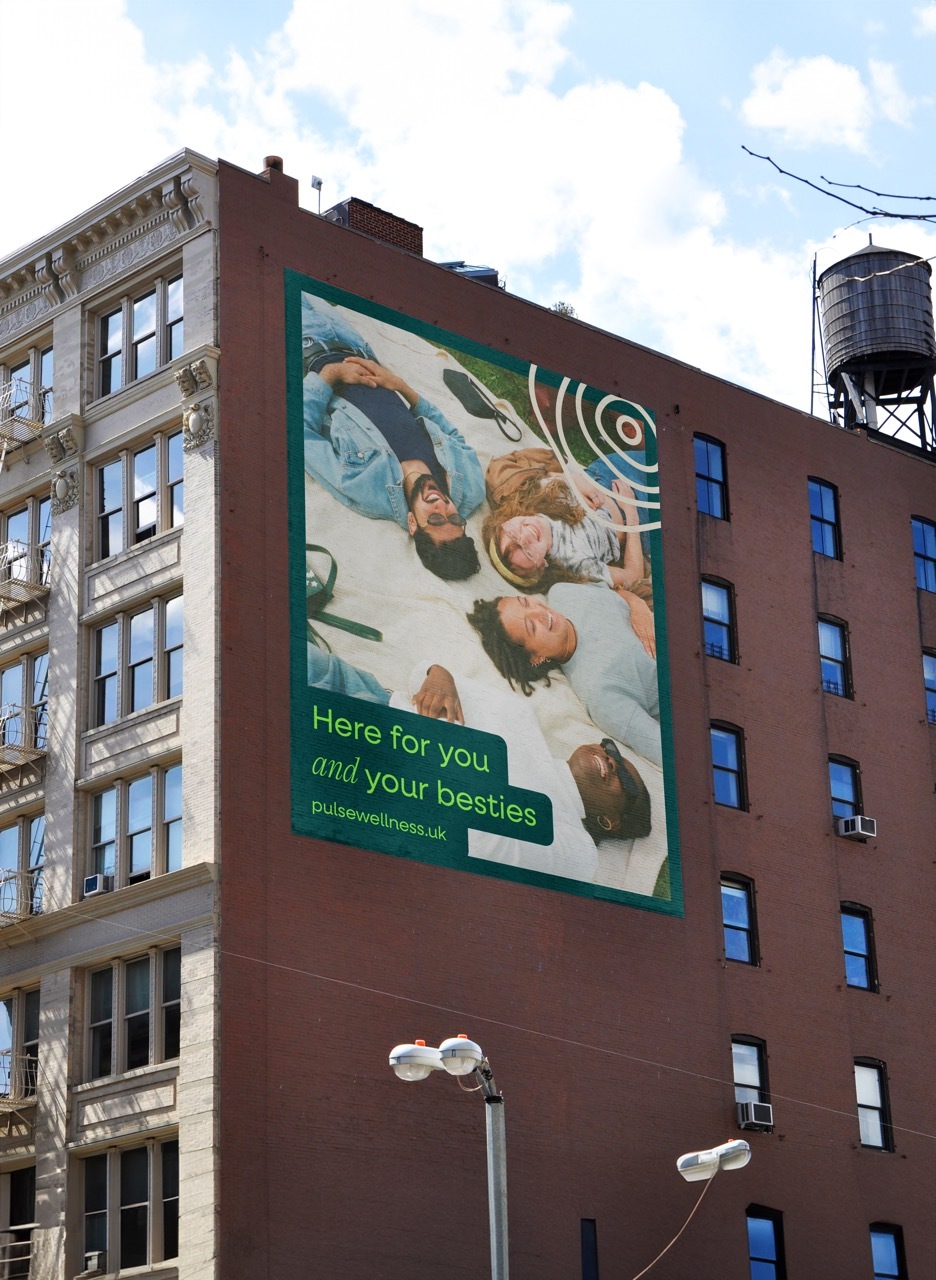 Mock-up billboard on the side of a building showing people laying down and green text that reads: 'here for you and your besties'.