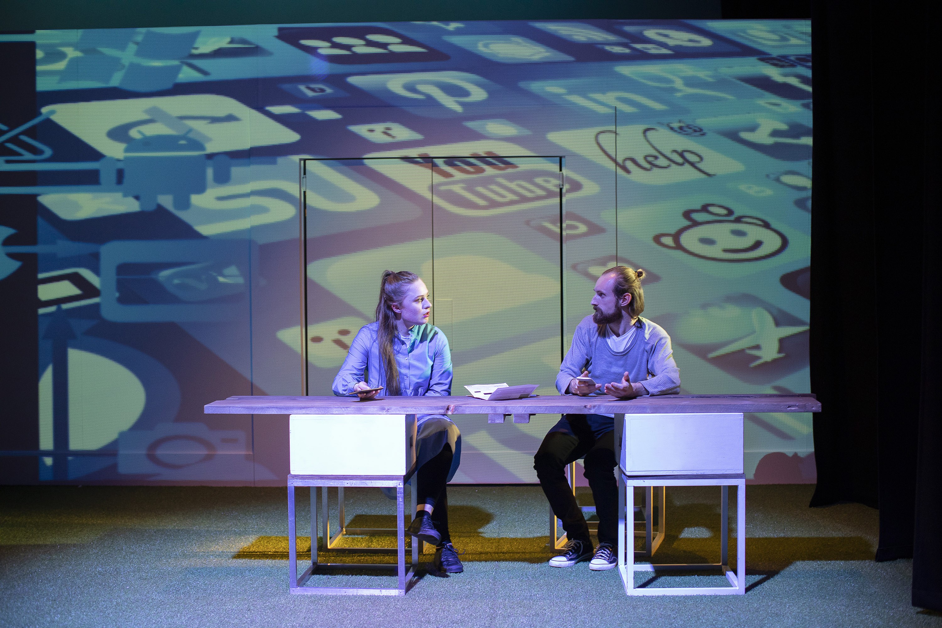 Two people sitting and talking behind a long table on a stage.