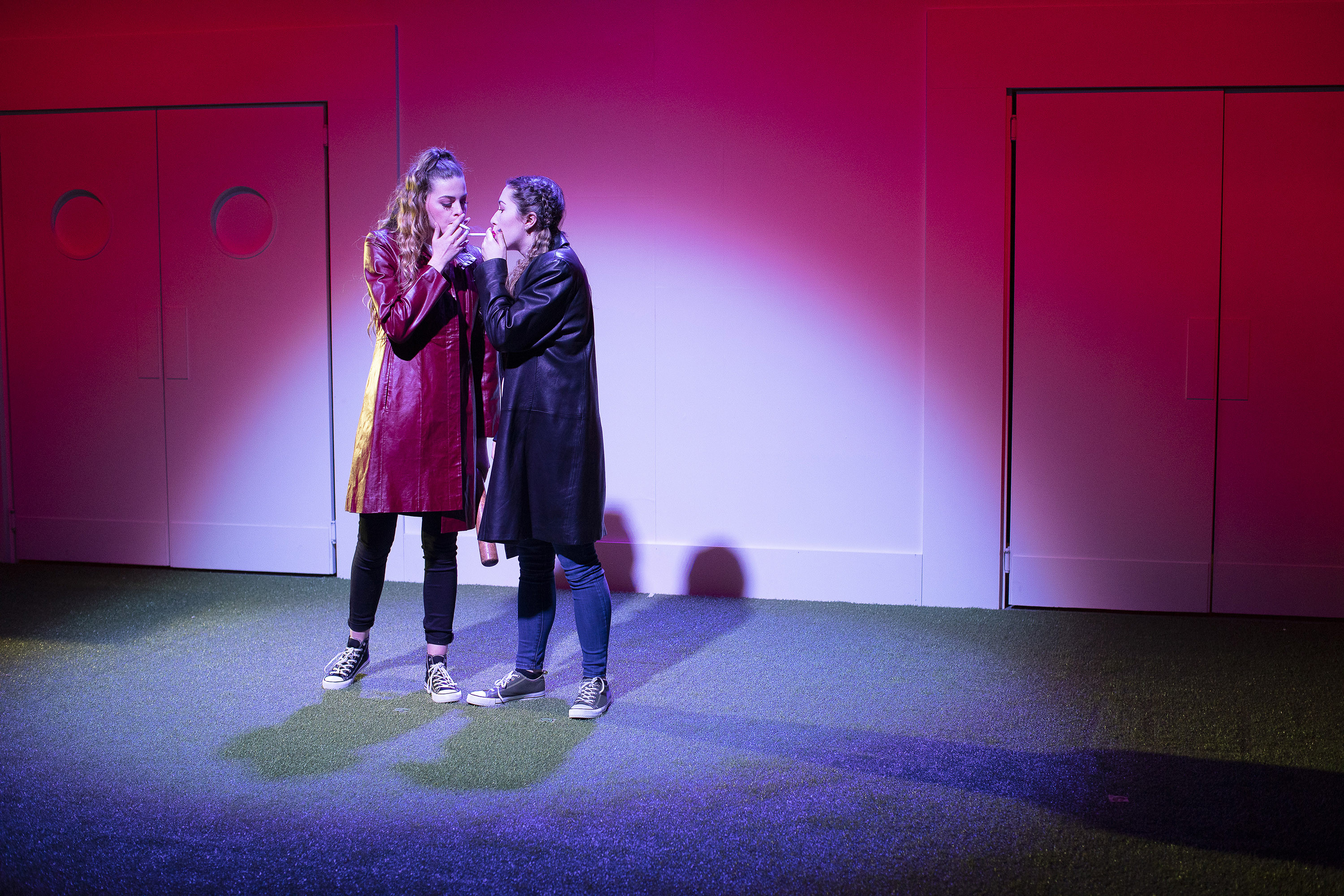 Two people standing on a stage holding cigarettes to their mouths.