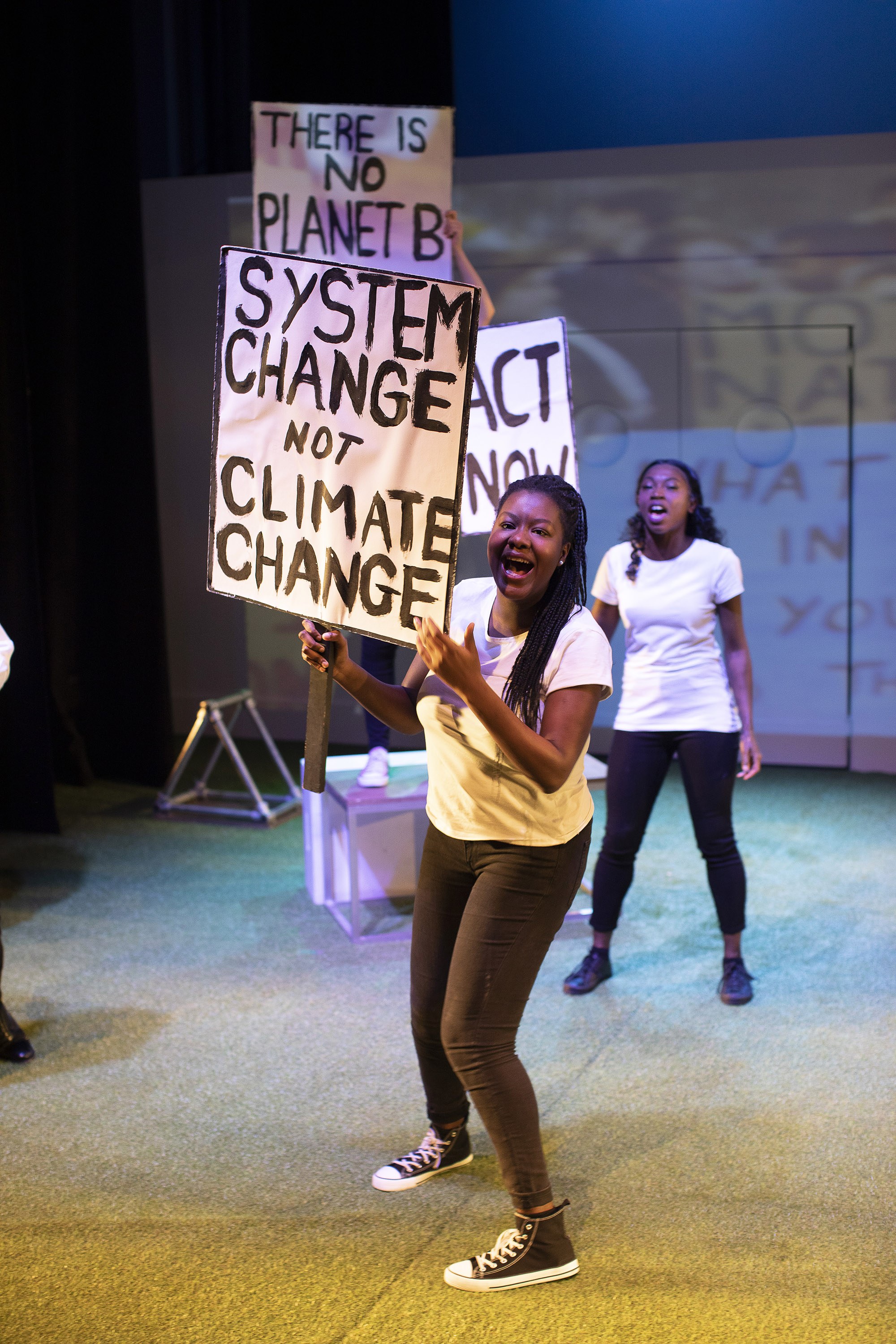 Two people standing on a stage holding placards in the middle of a protest. The placard of the person closest to the front reads "System change not climate change."