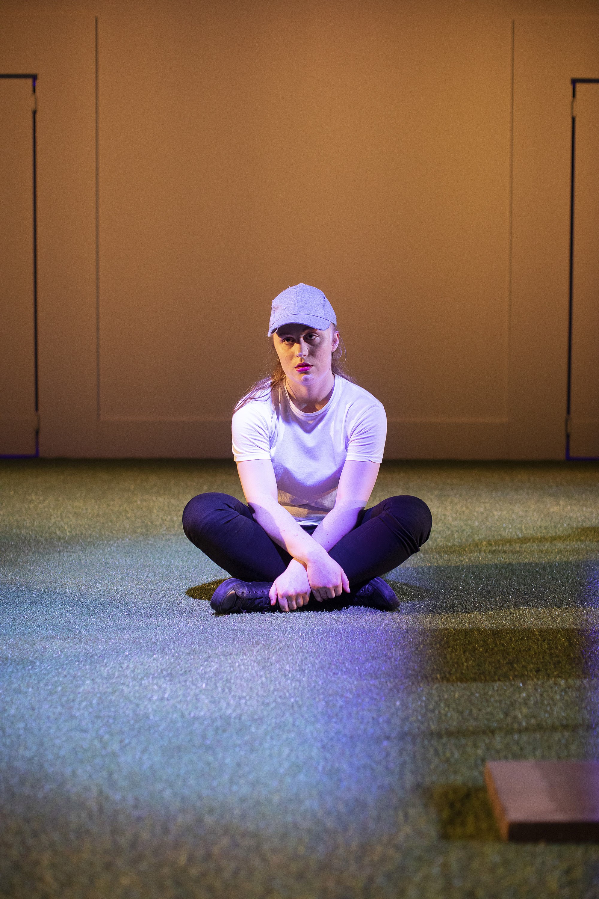 A person sits cross-legged alone in the middle of a stage.