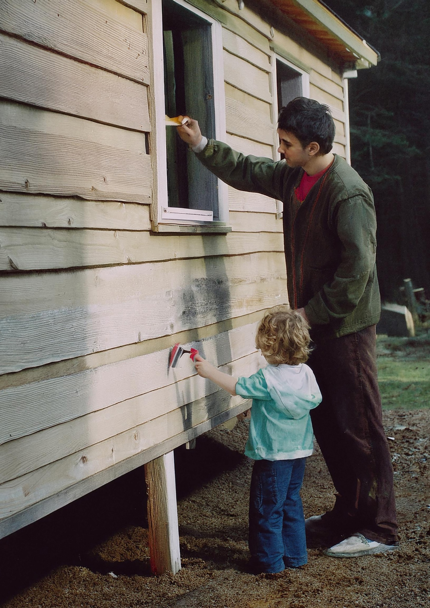 An adult and a child both standing and painting the outside of a wooden building.