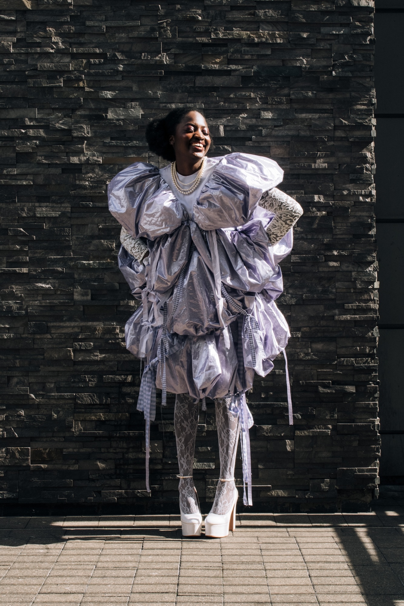 Model wearing a puffy layered purple-grey dress, smiling and turning slightly away from the camera.