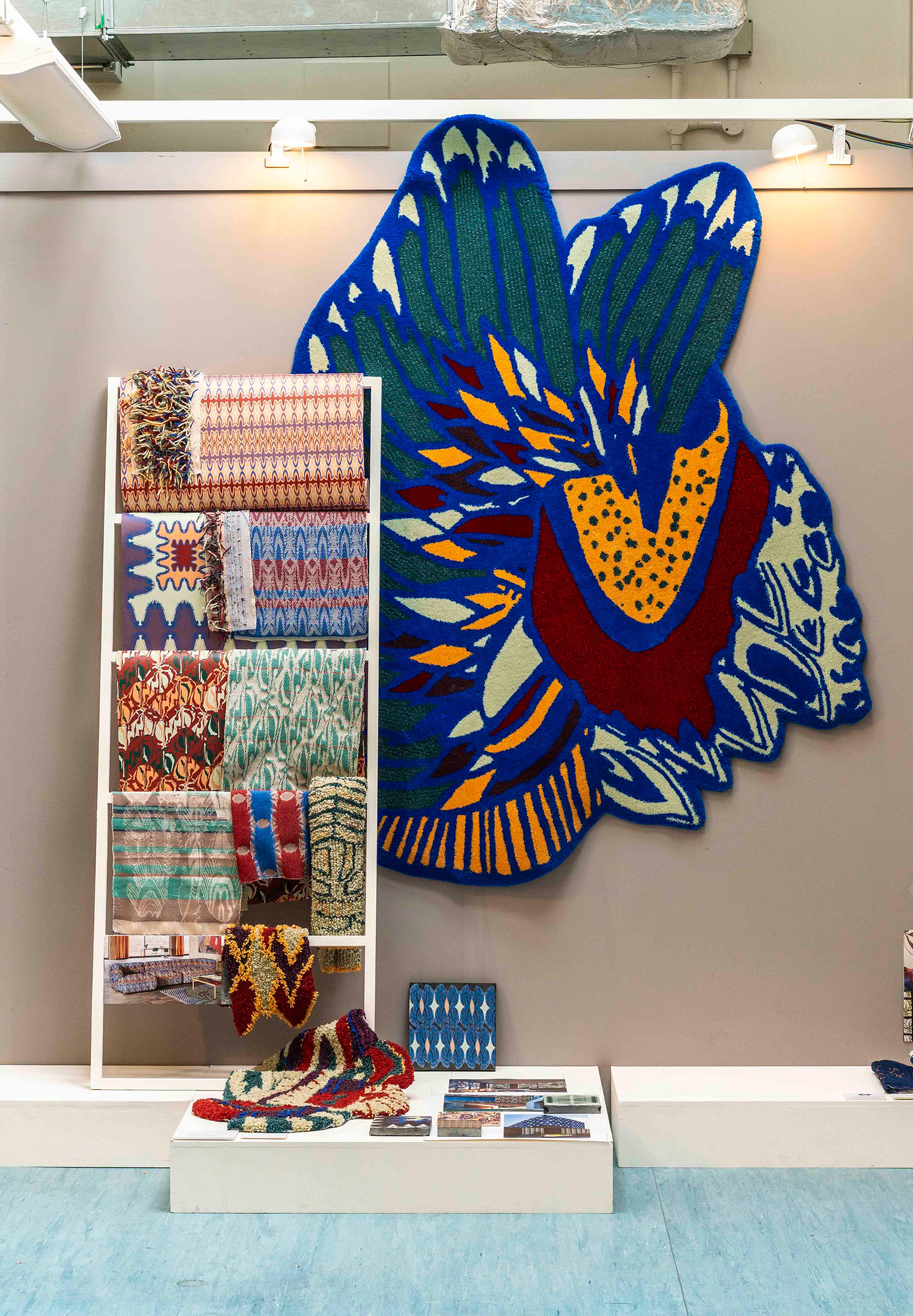 A large colourful fabric insect hangs behind a frame holding an assortment of rolls of fabric