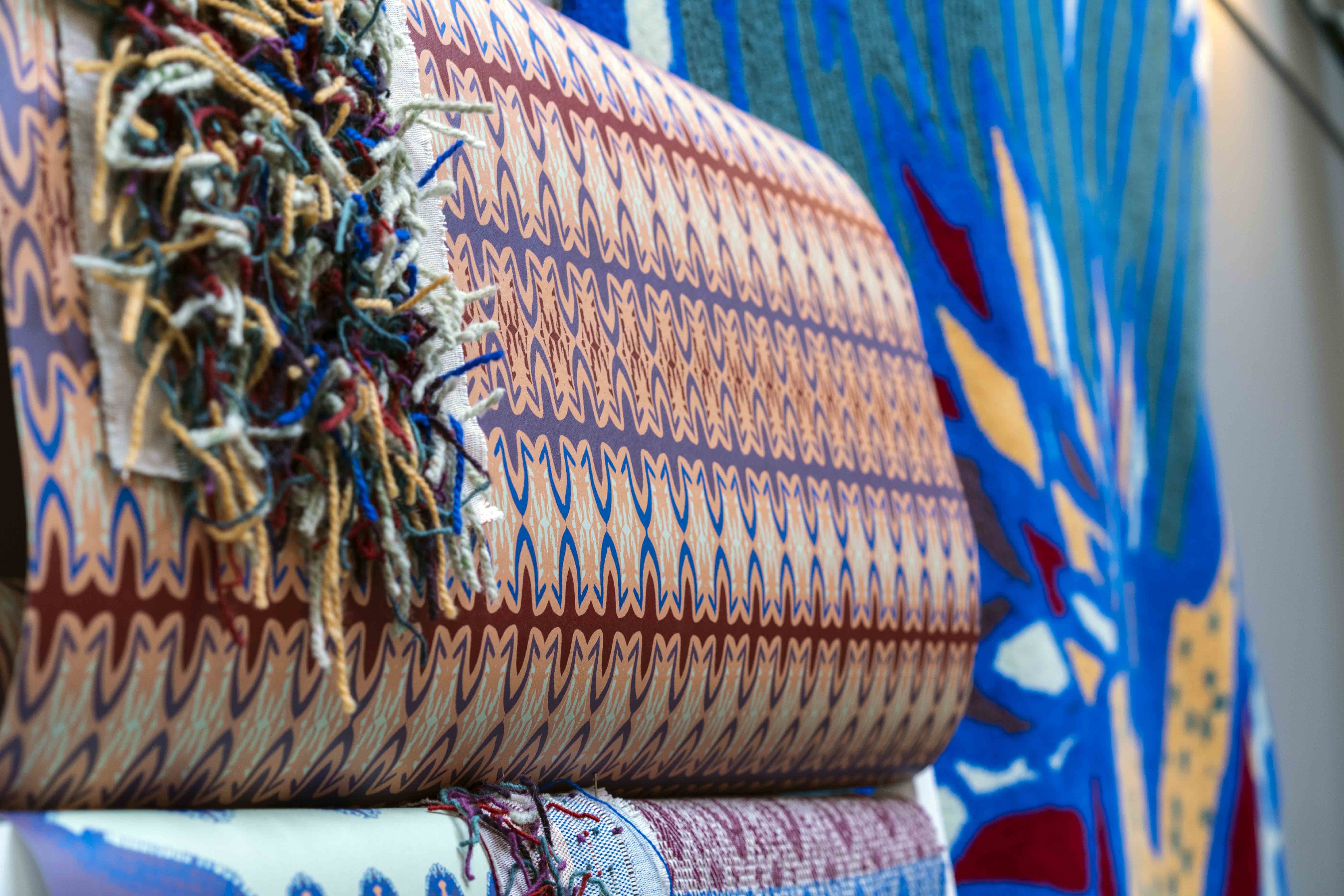A roll of opulent and colourful patterned fabric with a small sheet of tassels hung over it