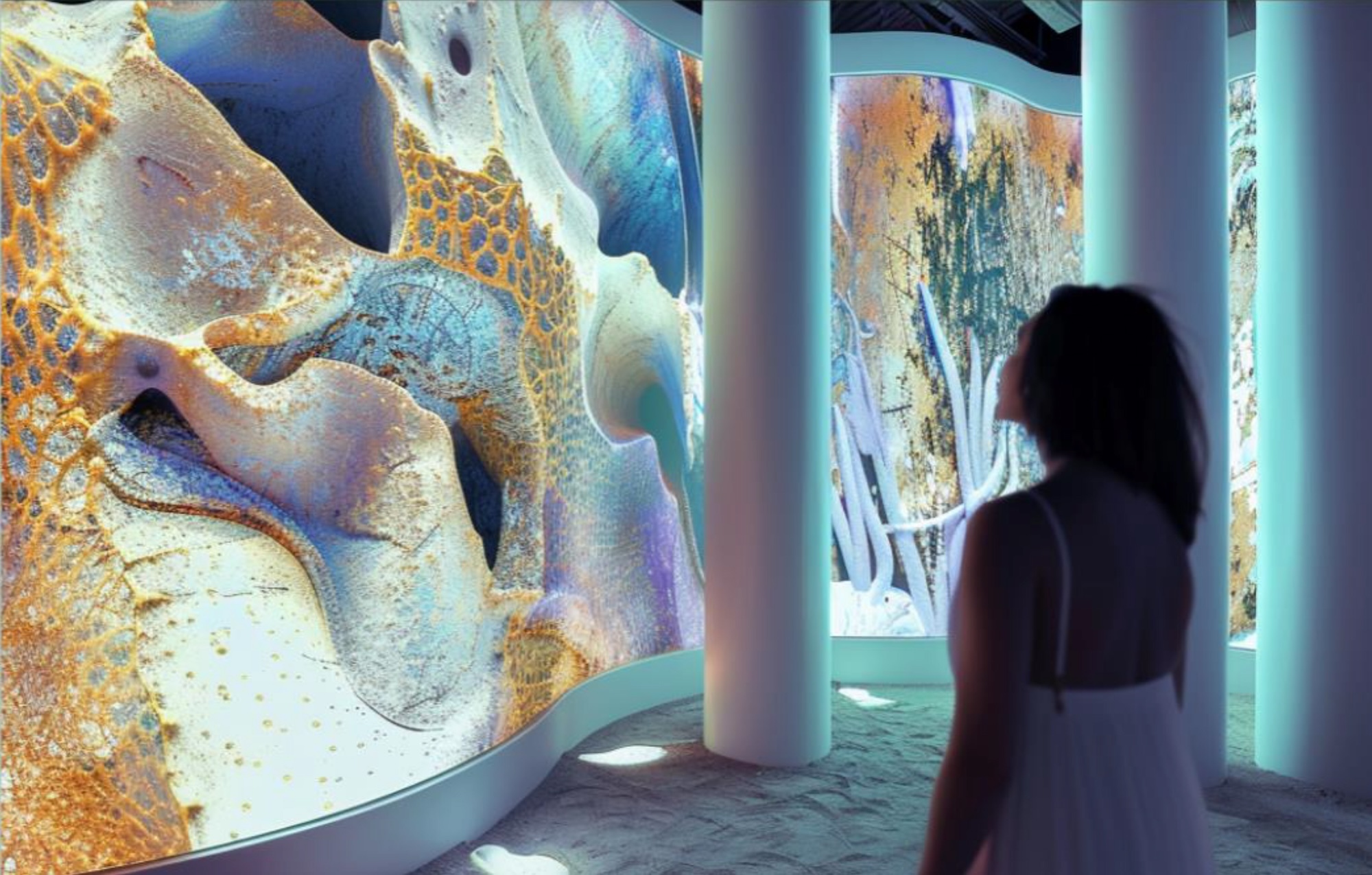 A woman in a bright aquarium-like room with wavy walls and pillars, decorated with a design resembling coral.