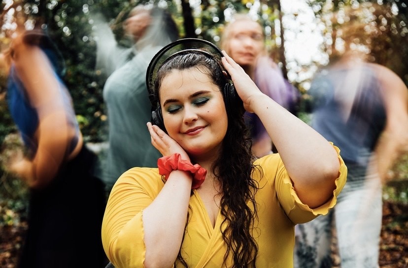 A dancer smiling outside in the rain wearing headphones and a yellow top.