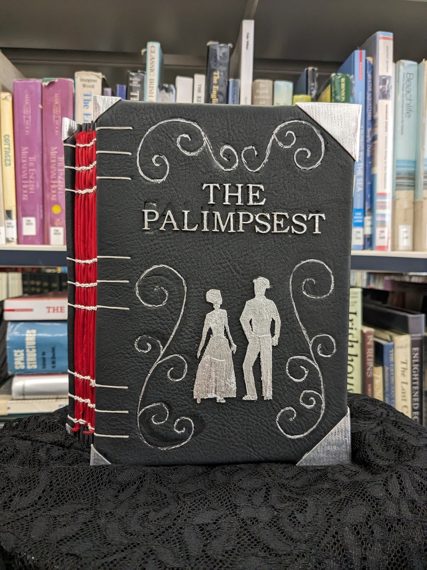 Handmade book with black cover and red spine binding. White text reads "THE PALIMPSEST" with decorative swirls and two figure silhouettes.