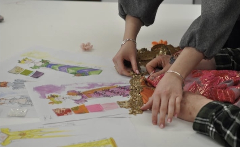 Hands working with colourful paper materials on white table surface, with craft supplies and decorative elements visible.