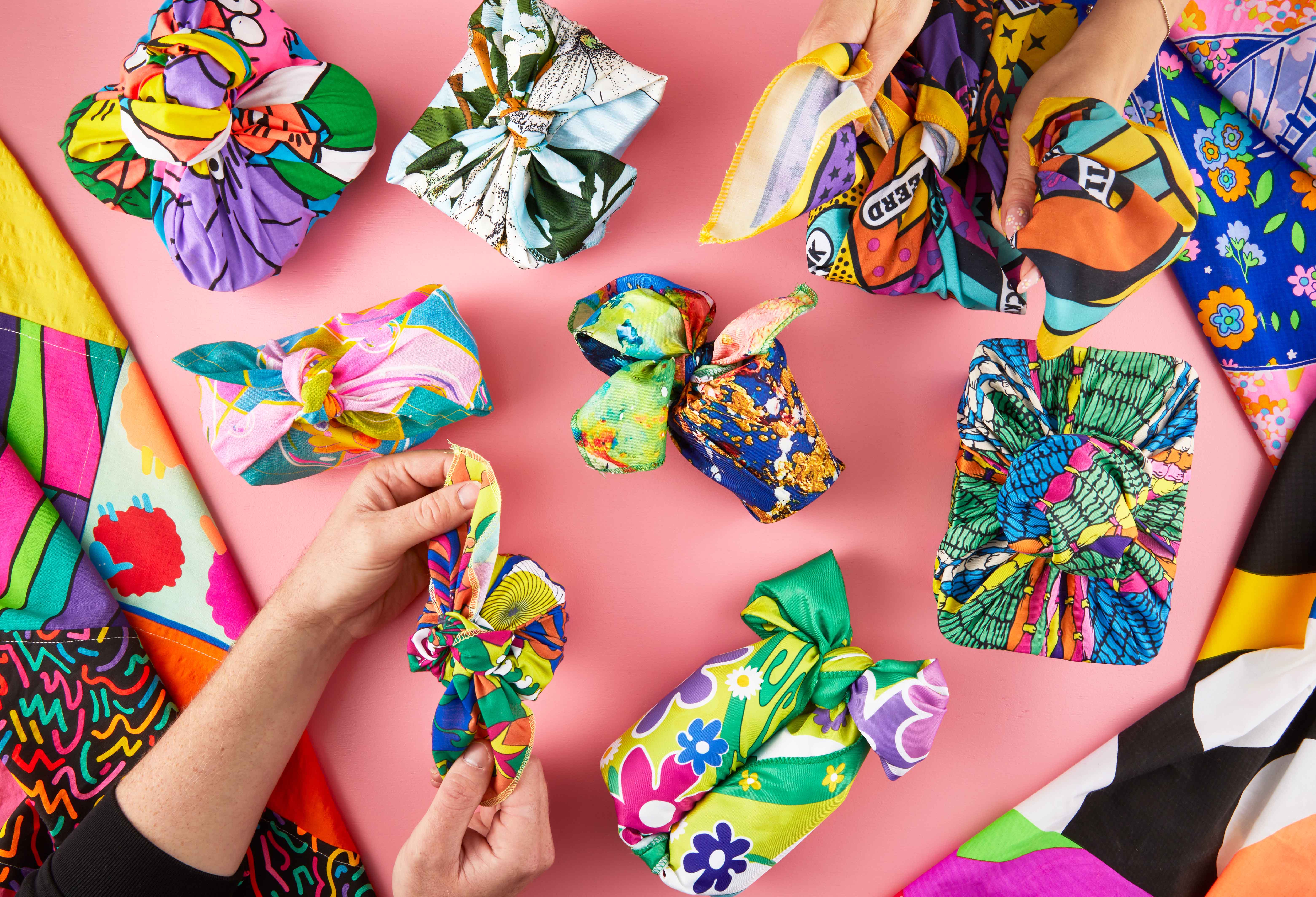 A selection of multicoloured Lush knot wraps on a pink surface, someone holding one of them