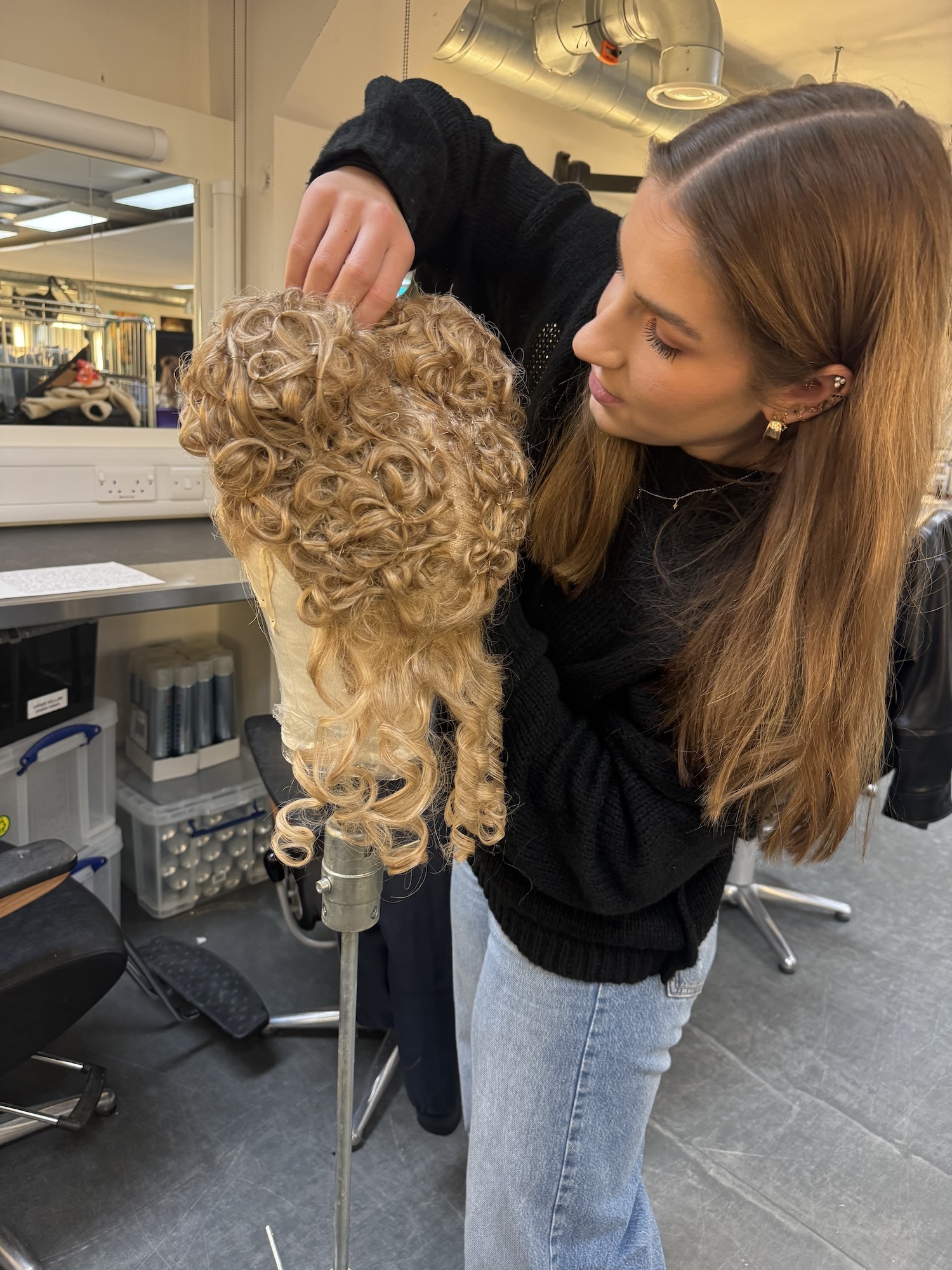 A BA (Hons) Make-up for Media and Performance student handling a 16th century wig on a mannequin head in a make-up studio.