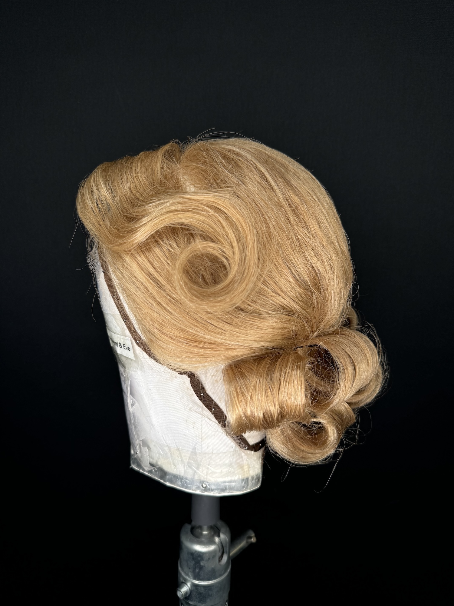 A wig of golden blonde curls displayed on a mannequin against a black background.