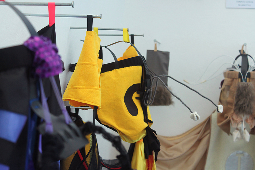 The apparel hung on 12-inch nails along the wall. Wasp’s yellow and black felt headpiece and antennae reach into the room towards the audience, flanked by Dung Beetle’s black and purple, and Moth’s neutral apparel.