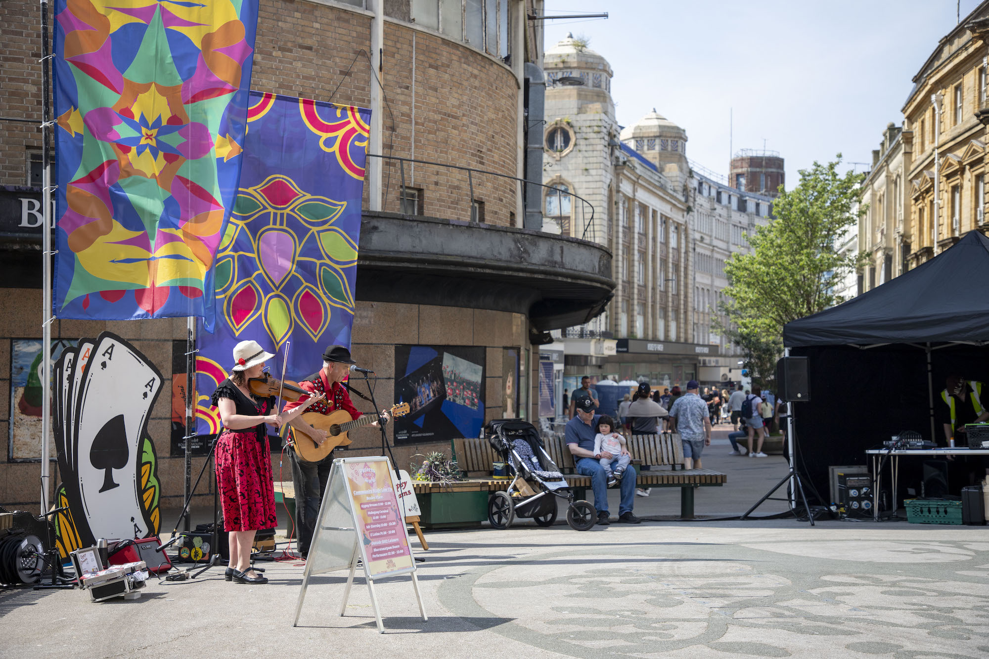 Musicians performing next to a playing card standee on Bournemouth high street during Alice in Spring 2024.