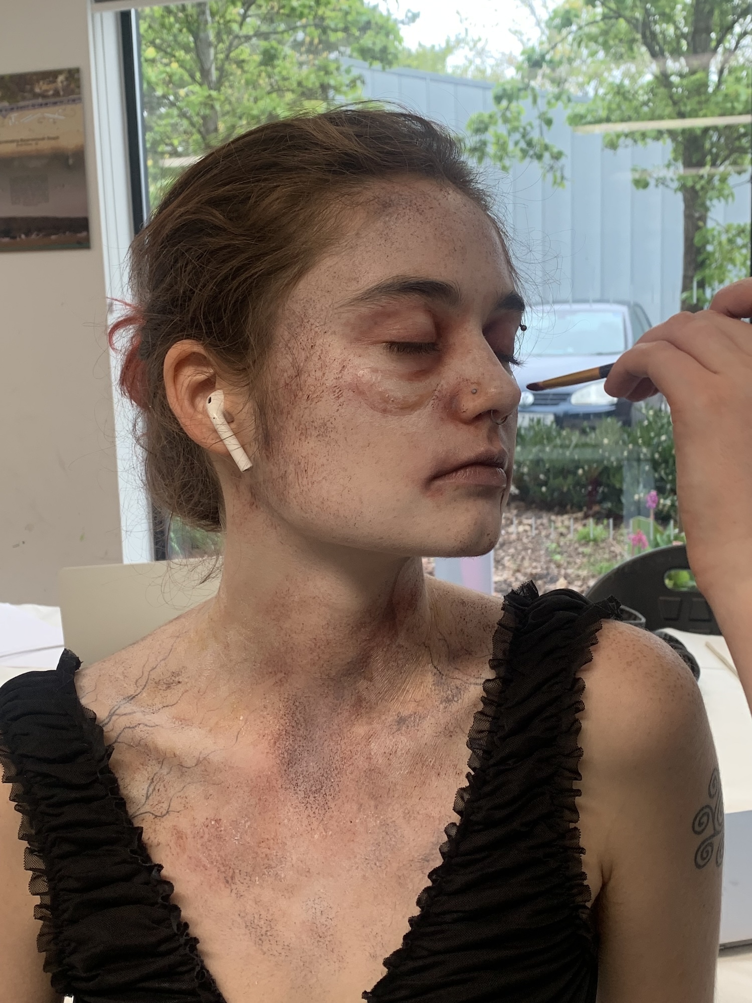 A Foundation Diploma in Art, Design and Media student sitting with their eyes closed having horror-style make-up applied by a fellow student off camera.