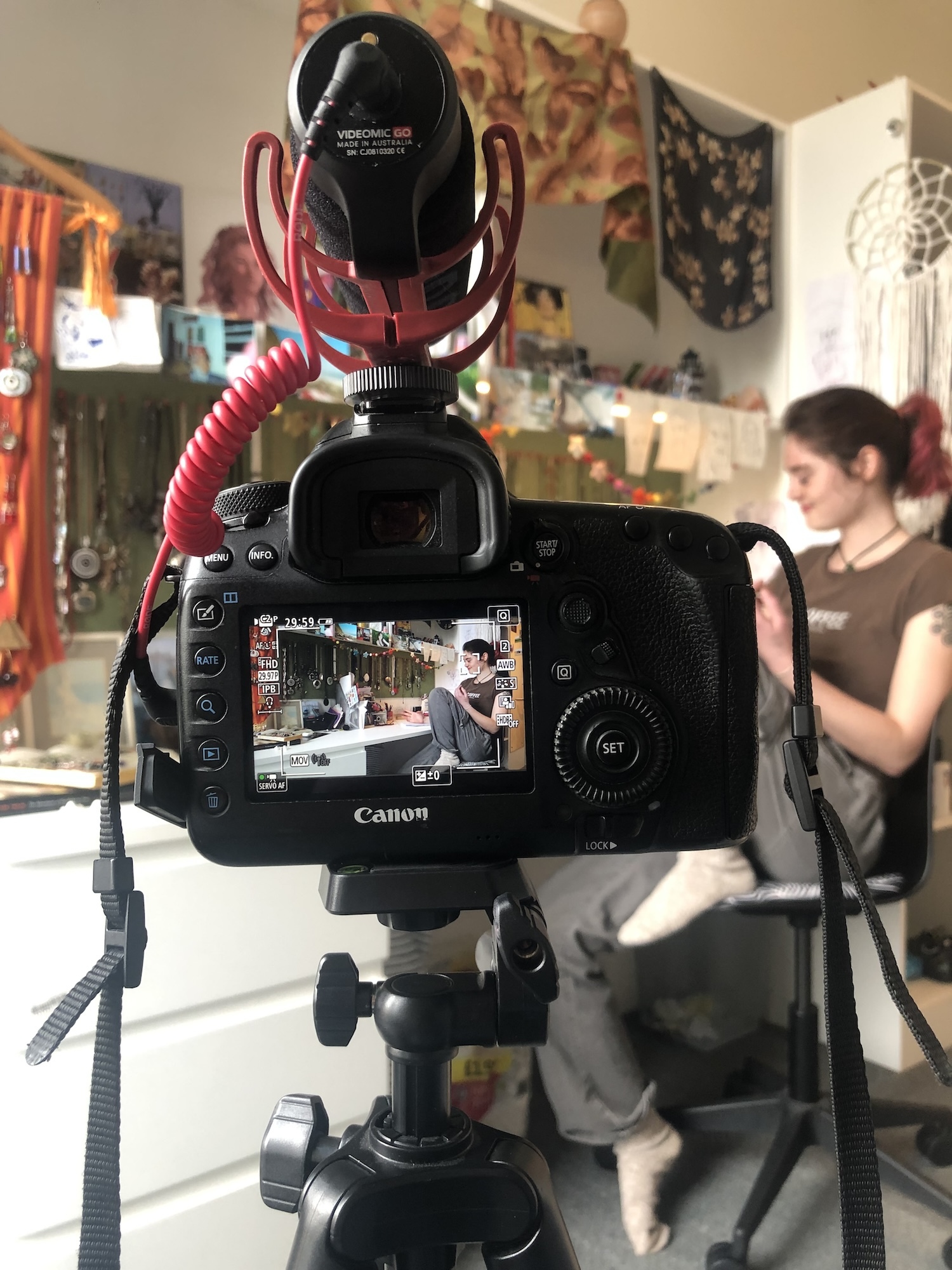 Close-up of the viewfinder of a Canon camera, showing a young person sitting in a workspace.