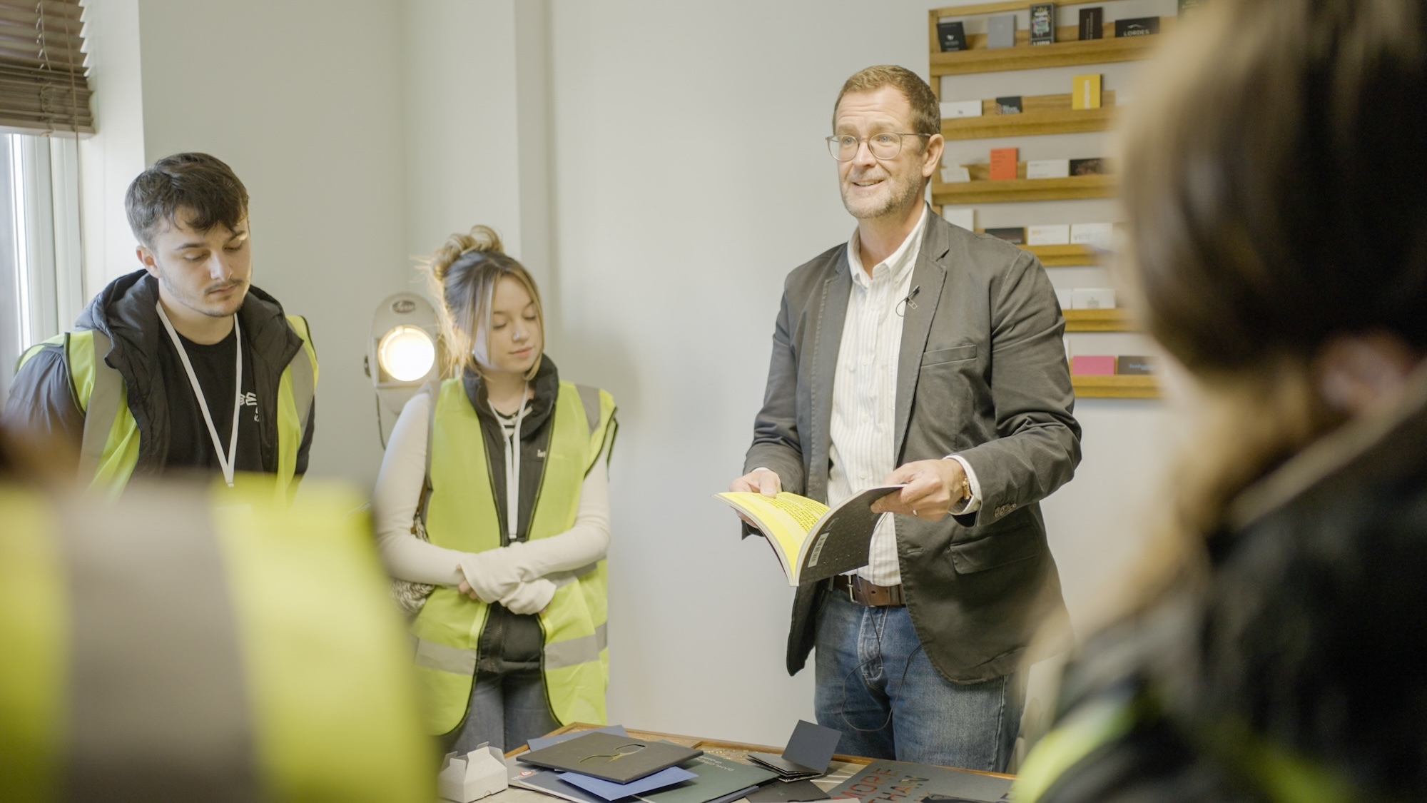 M Smith from Dayfold holding a document standing next to two AUB students while delivering a workshop.