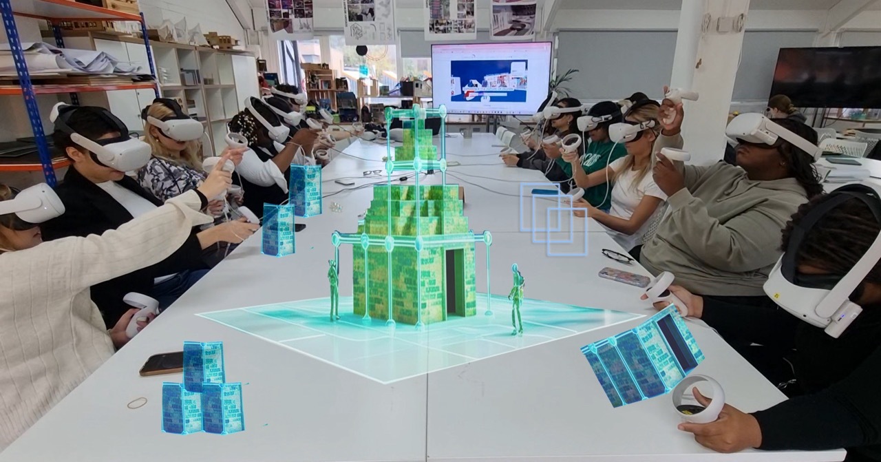 Students around a table wearing white VR headsets, in the middle are 3D blue and green structures, representing what students are seeing through headsets.