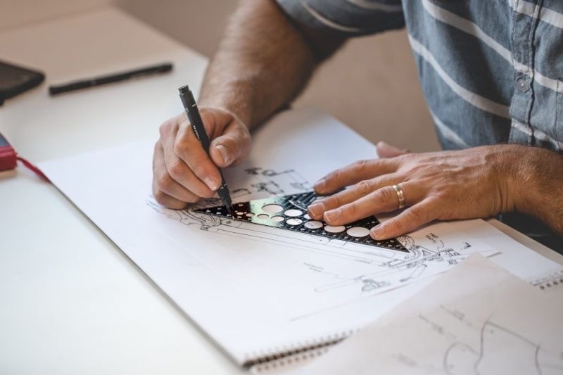 Person holding a complex ruler drawing designs on paper with a pencil.