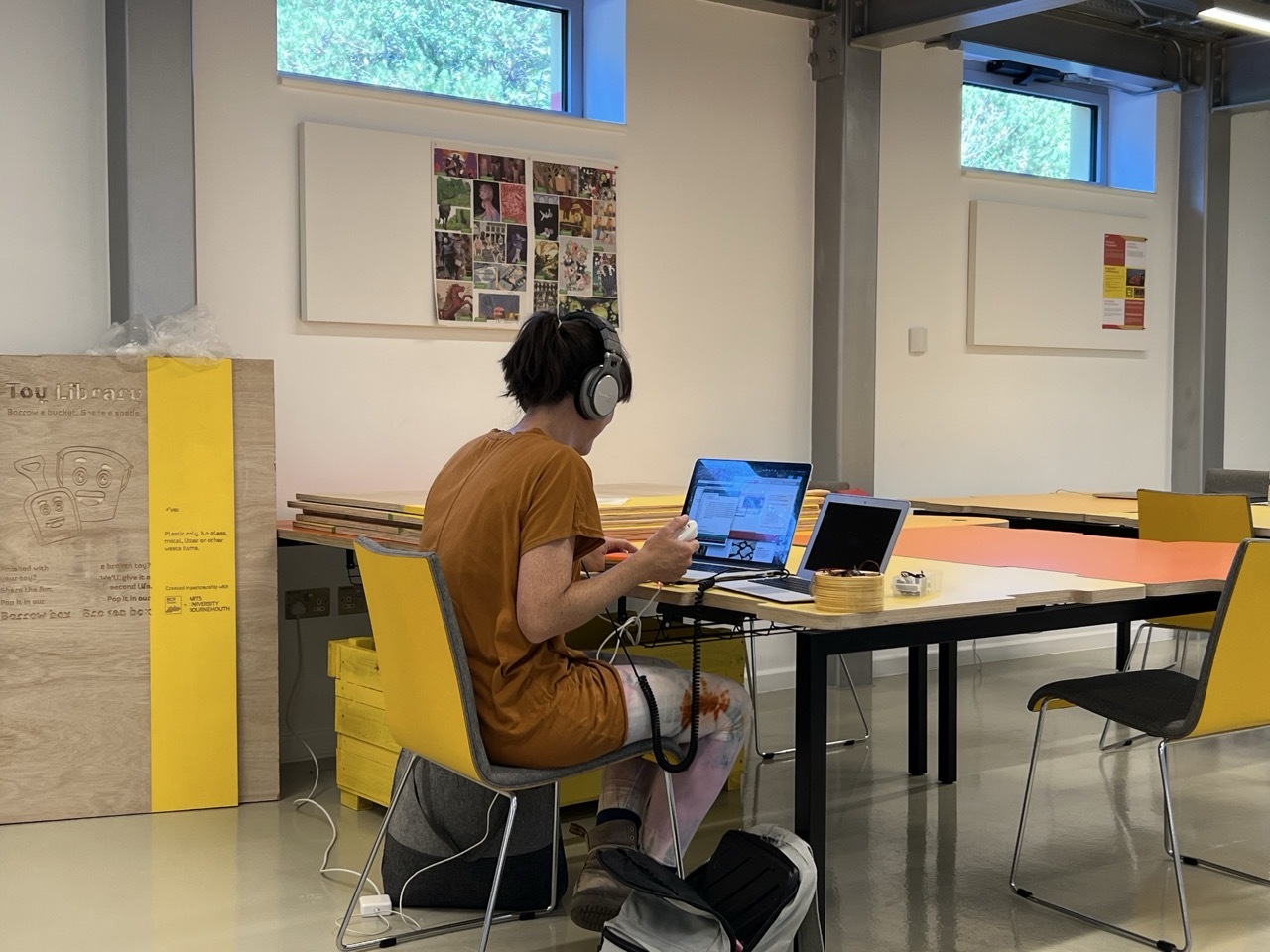 Student working in the Innovation Studio with headphones on, sat at an orange desk with yellow seats.