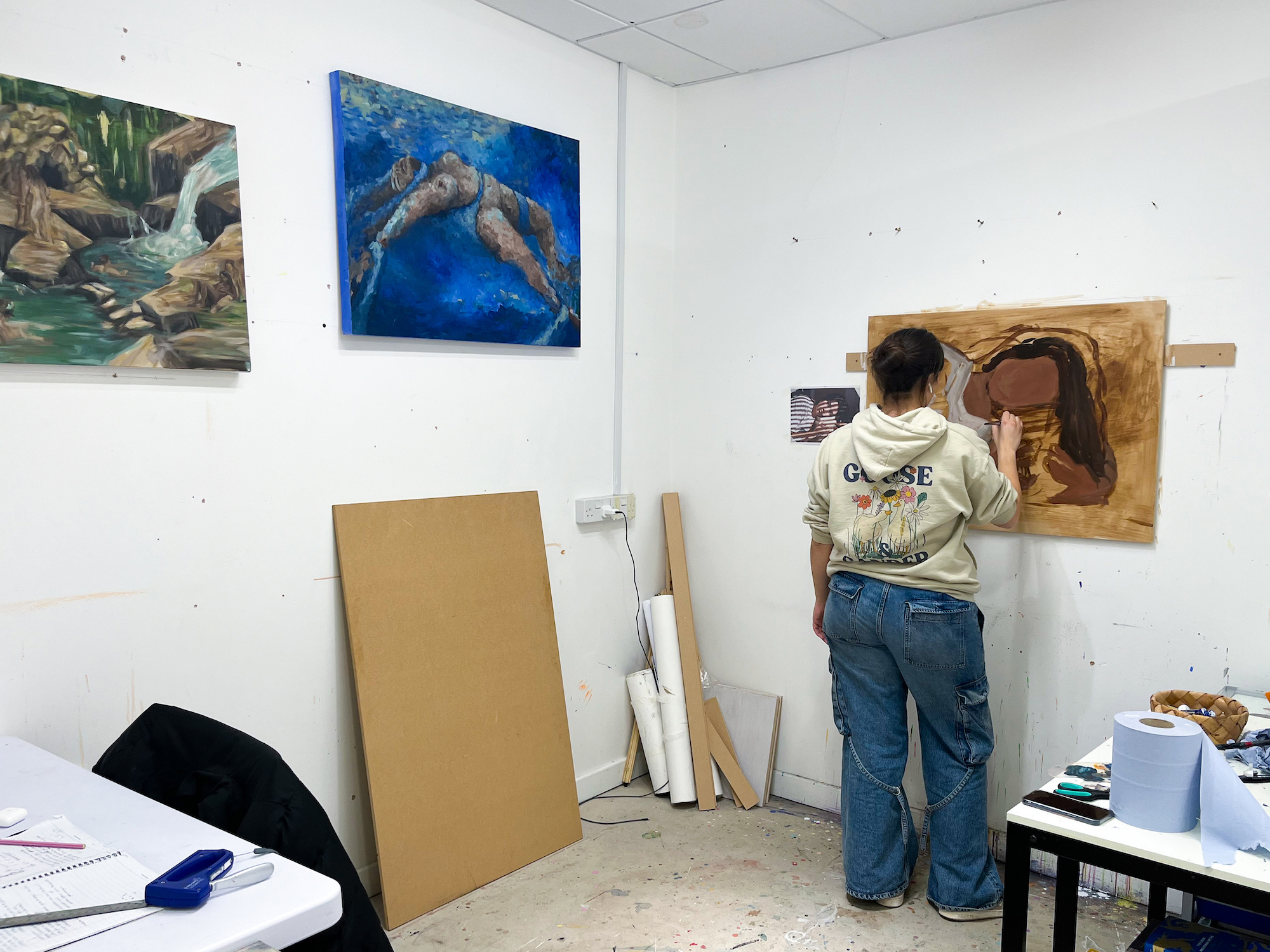 A student painting on a wall-hung canvas in a studio space.
