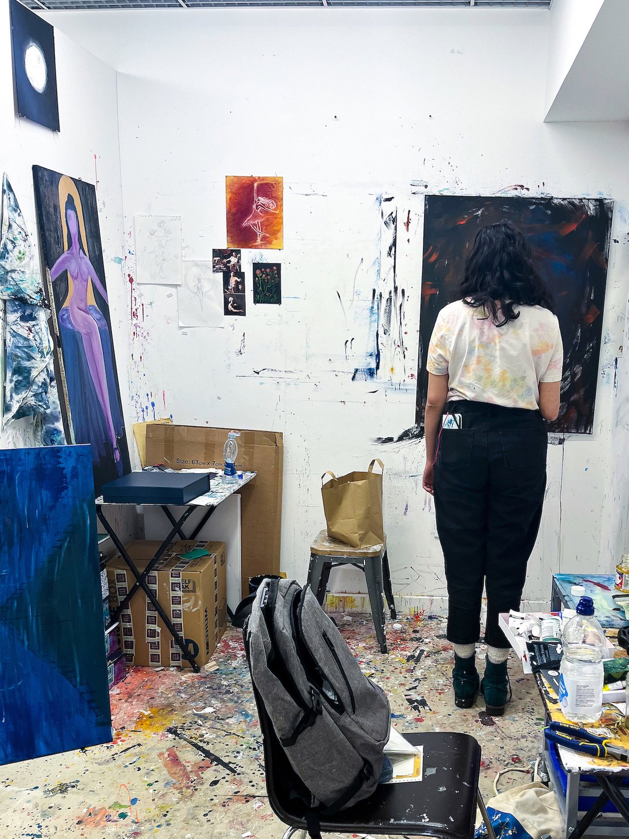 A student painting in a messy studio space, with paint on the walls and floors.