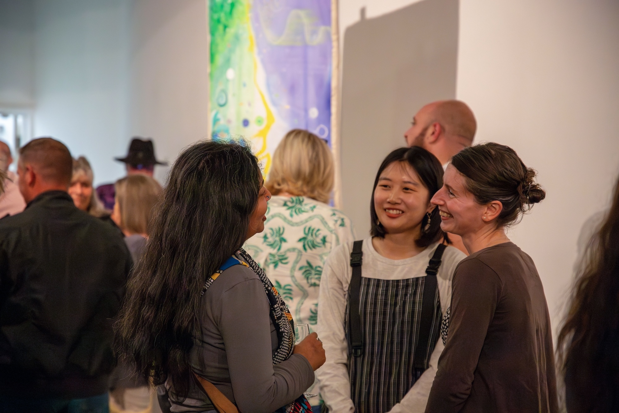 Three people speaking in a crowded gallery space during AUB's MA Painting 2024 show at Poole Lighthouse.