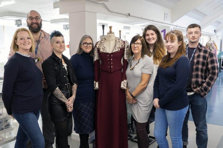 A group of people stand and pose for a photo. A mannequin in costume is stood in the centre.