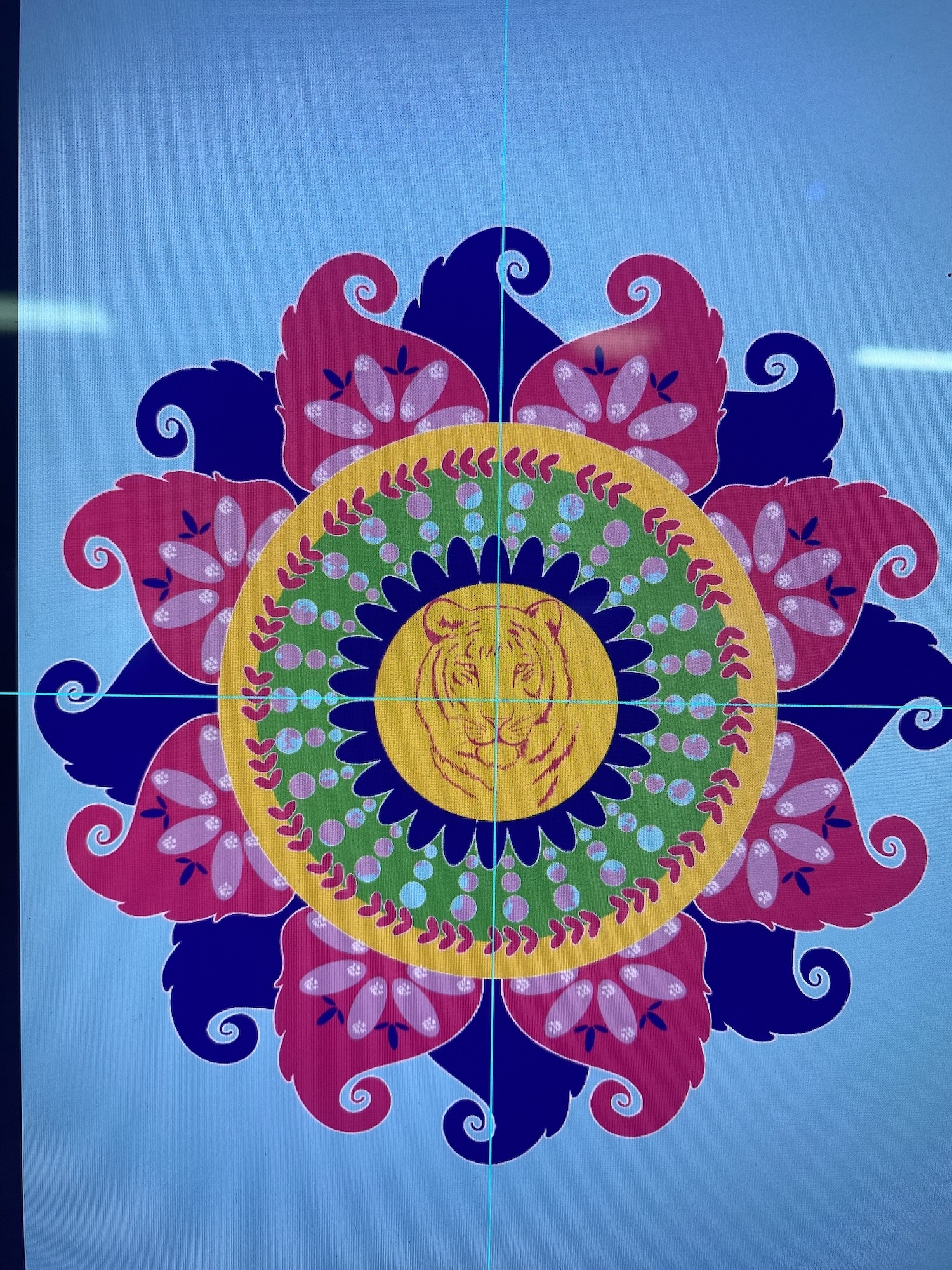 Colourful mandala design with central yellow circle containing tiger face, surrounded by concentric rings of green, blue, and red decorative patterns on blue background.