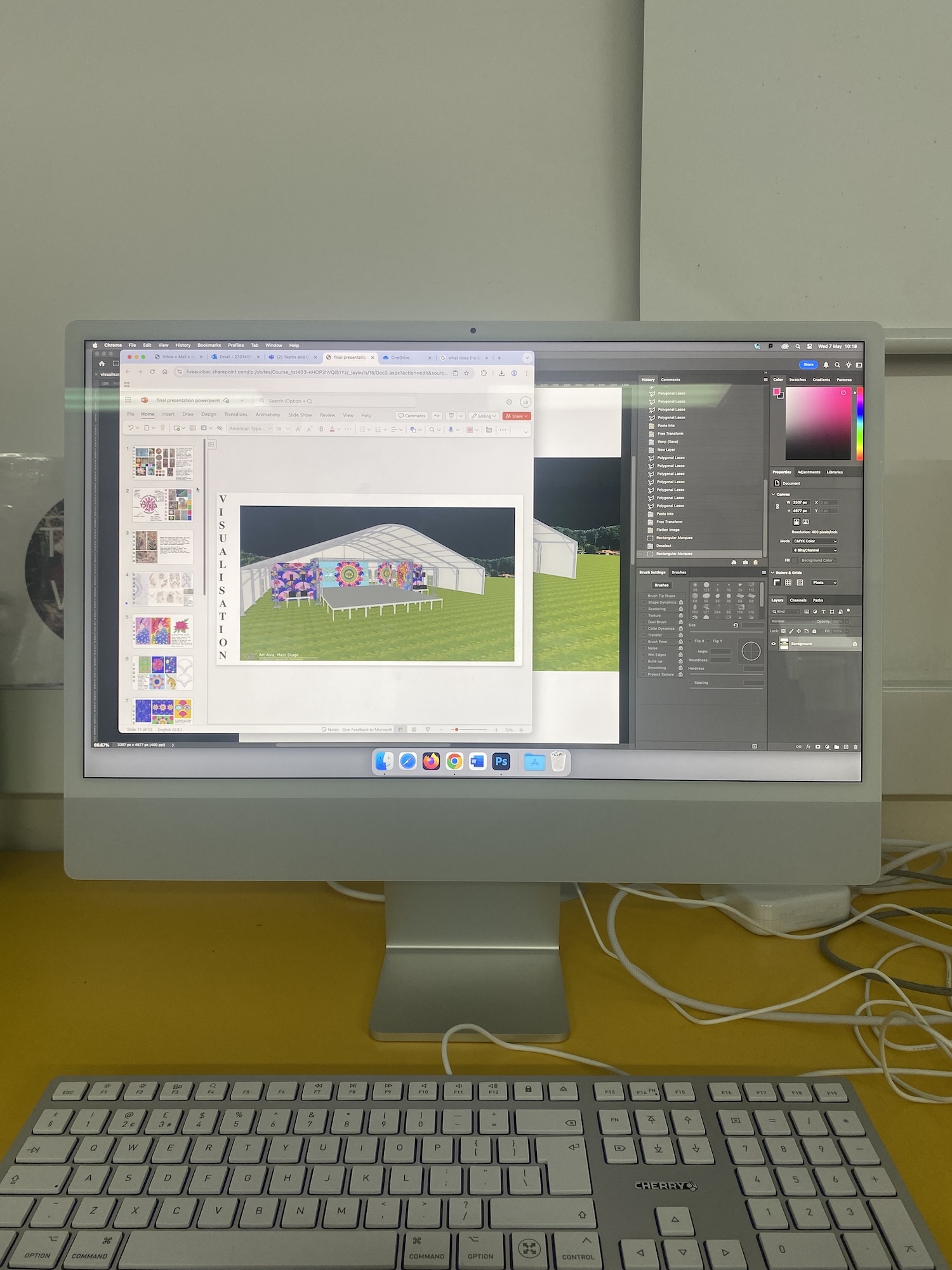 Desktop computer displaying Photoshop with tent design on green background, white keyboard and cables on yellow desk surface.