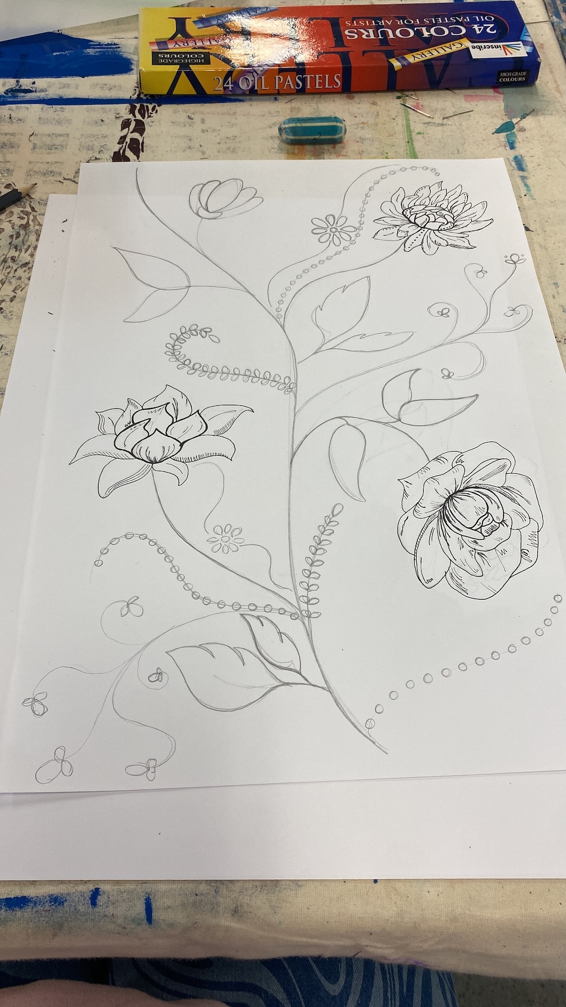 Pencil sketches of flowers and curved stems on white paper, with oil pastel box and art supplies visible on desk surface.