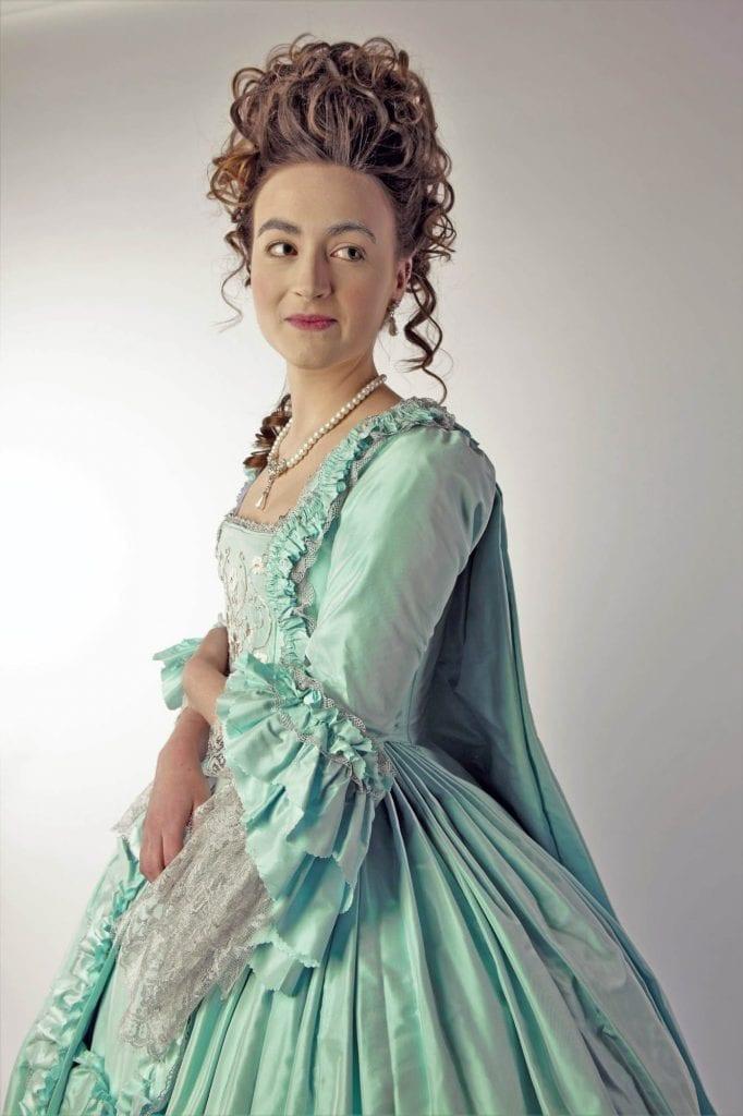 Model in a period dress and hairstyle poses for a photo.