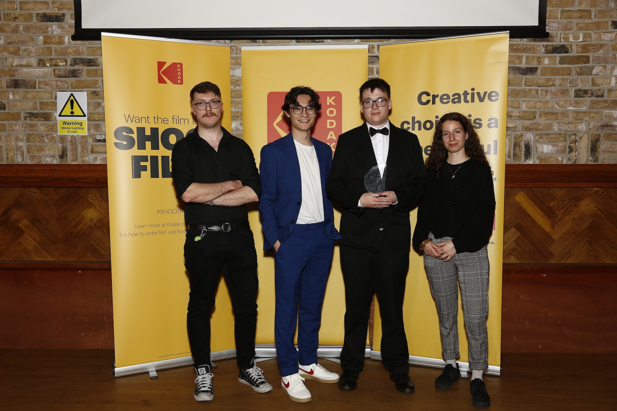Four BA (Hons) Film Production students from Arts University Bournemouth pose for a photo in front of three yellow banners at the Kodak/NAHEMI Student Commercial Awards 2025.