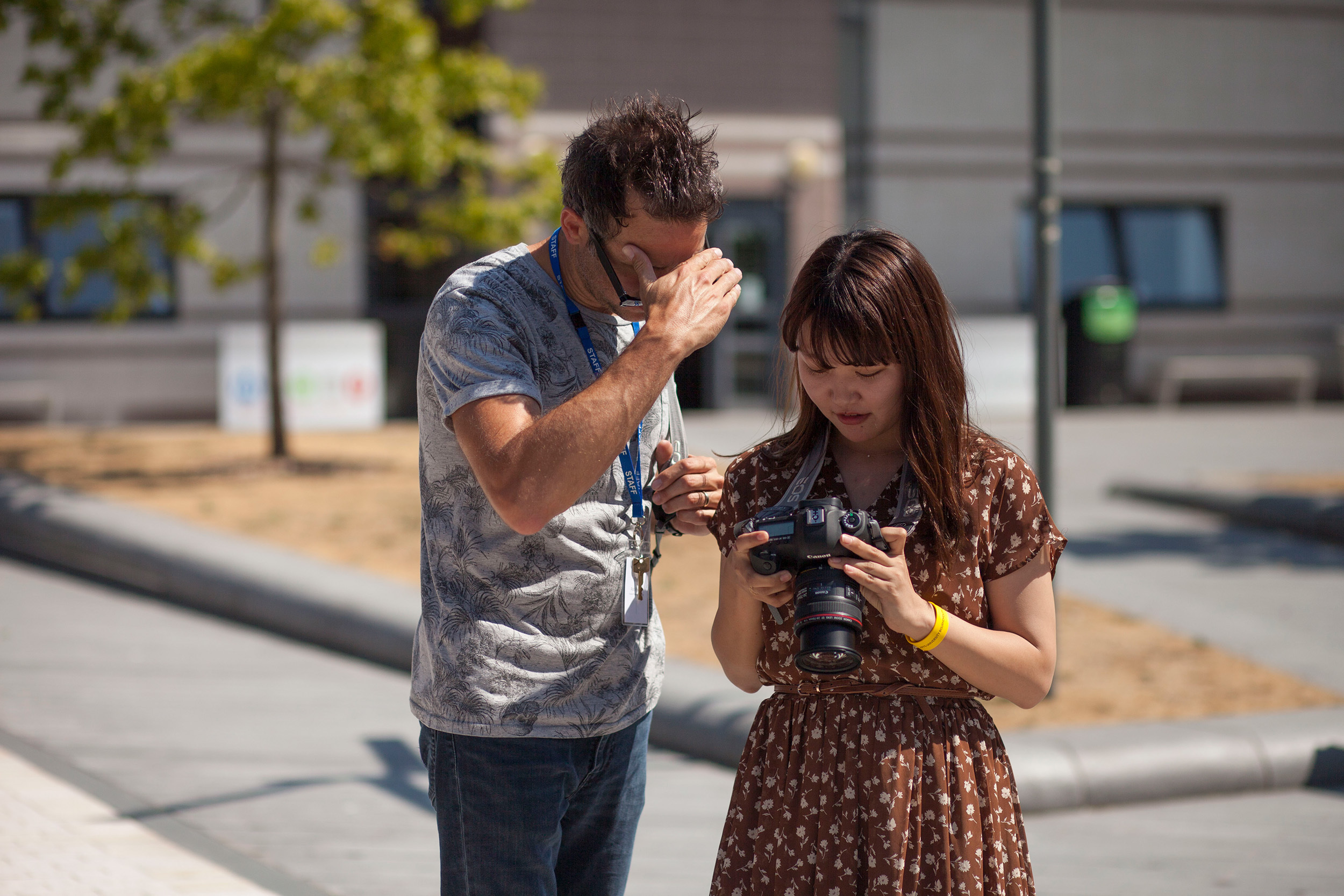 Two people standing in a university courtyard looking at a DLSR camera.