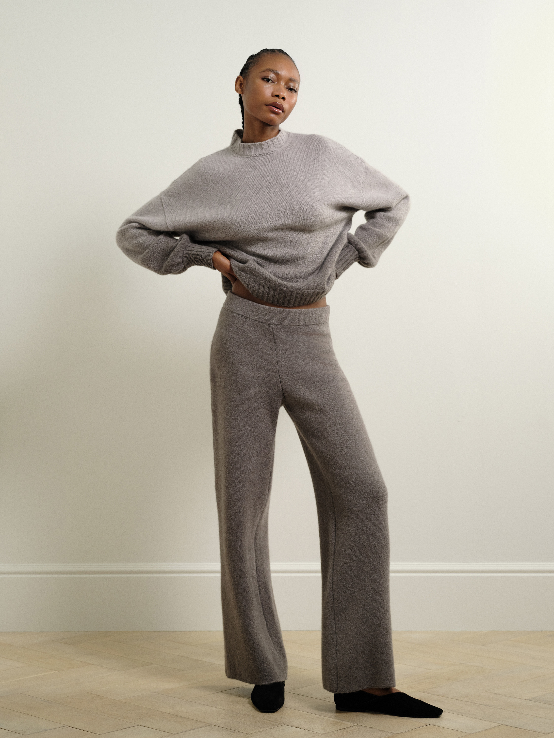 A model posing in a grey woollen outfit. The model is lifting the top up slightly.