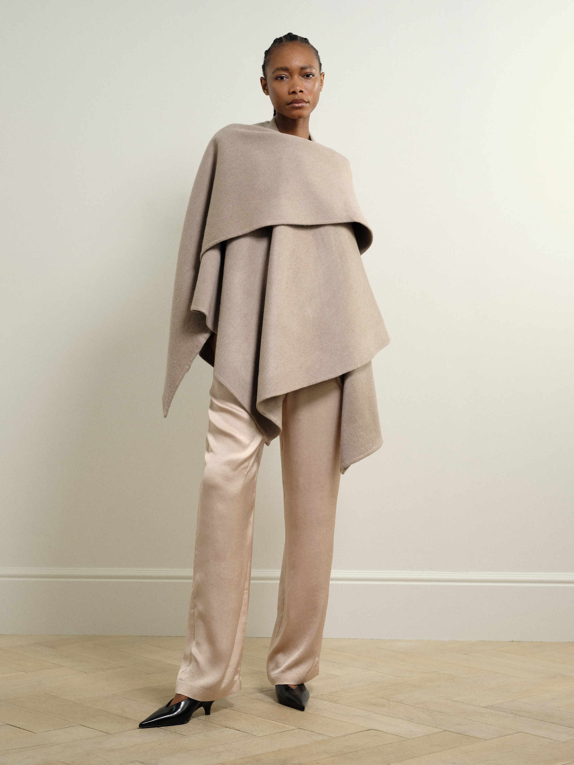 A model posing while wearing a long woollen shawl draped around their upper torso and satin trousers.