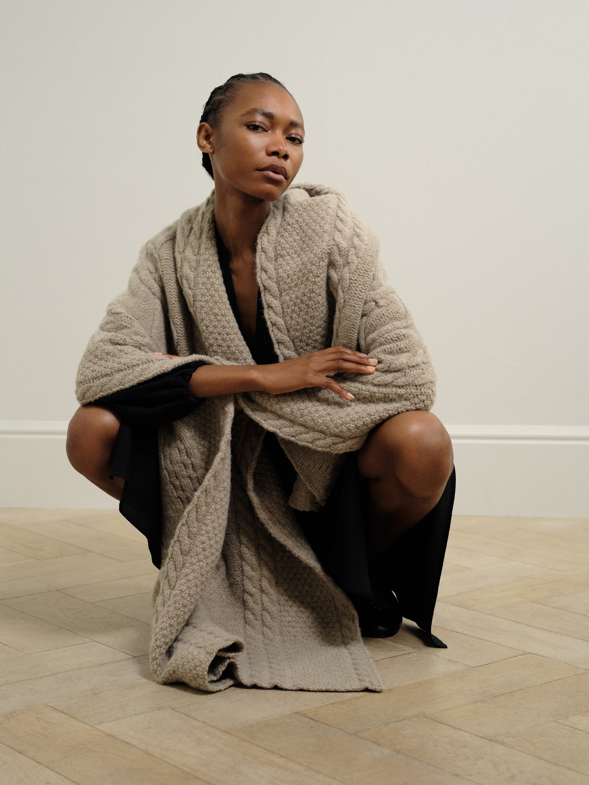 A model crouches down and poses for a photo while wearing a long, grey woollen garment.
