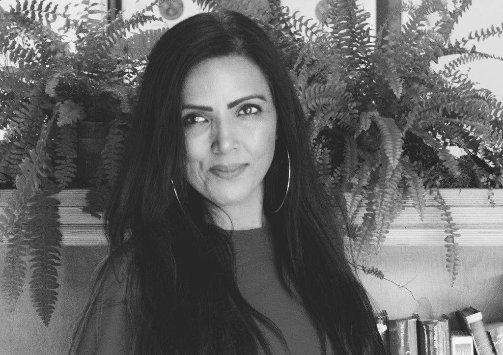Woman with long dark hair smiling at camera, ferns and foliage in background, black and white portrait.