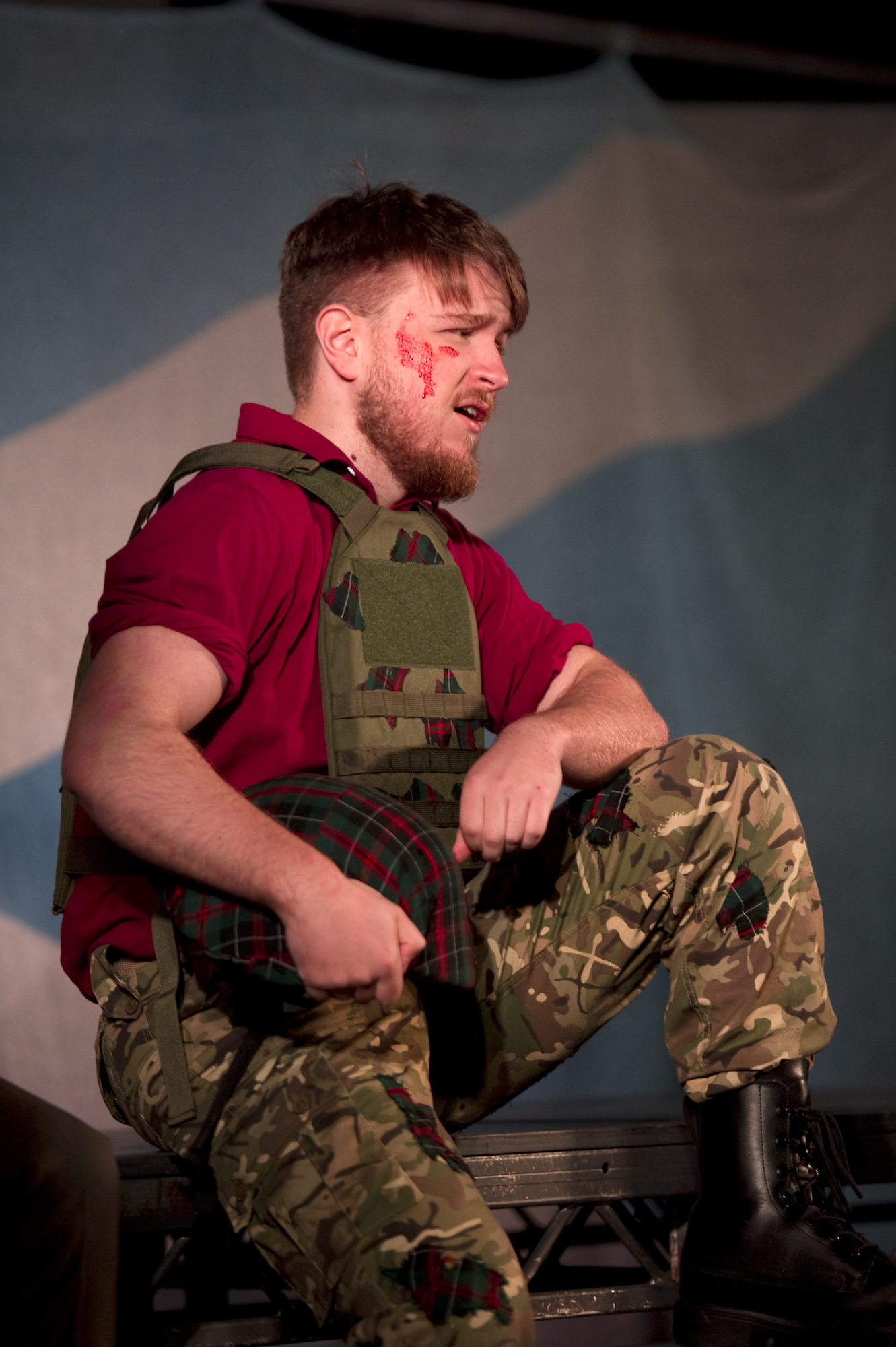 A BA (Hons) Acting student dressed in military fatigues sitting on stage performing Macbeth.
