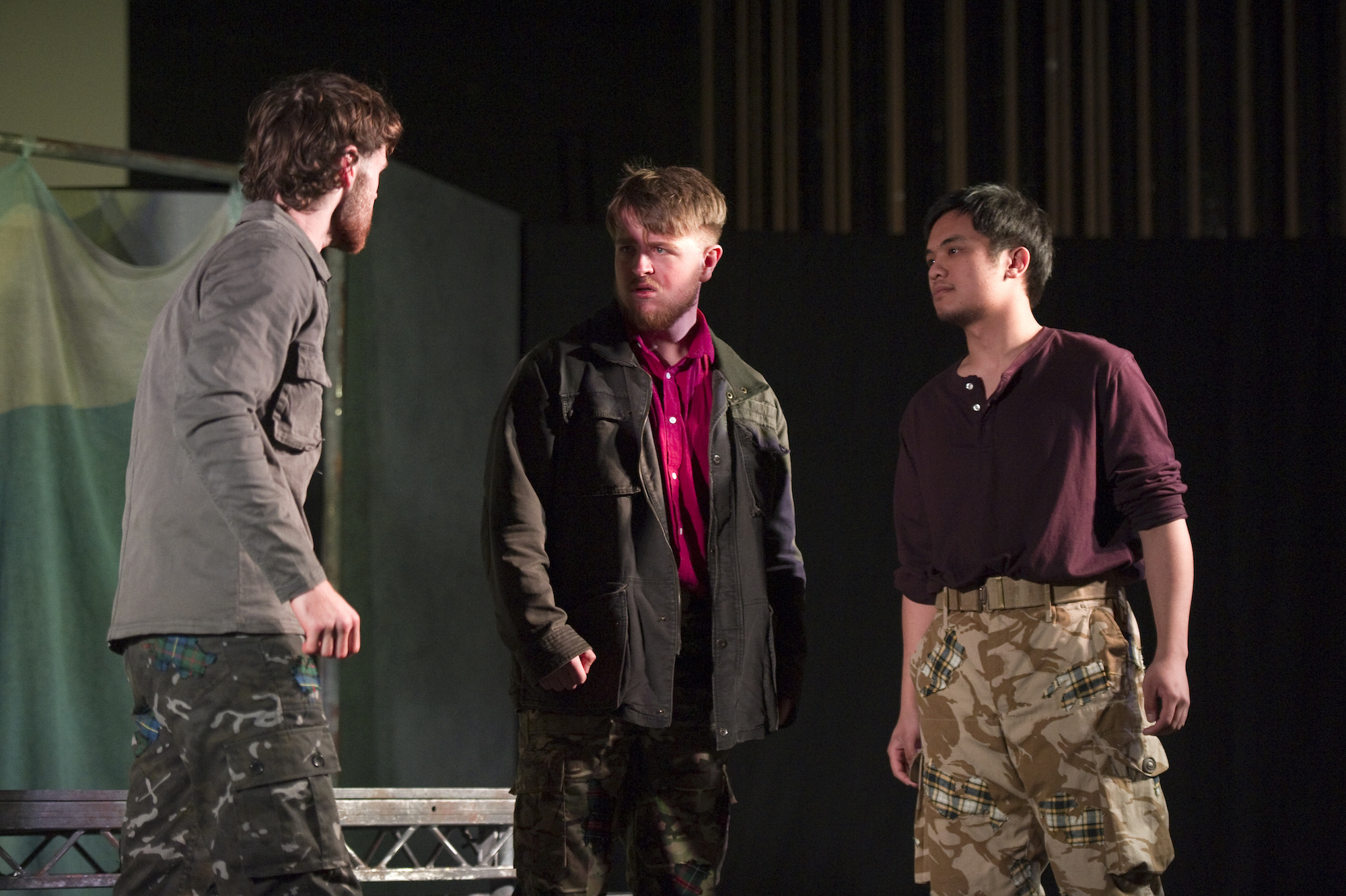 Three BA (Hons) Acting students on stage at Palace Court Theatre performing Macbeth. One performer with his back to the camera is speaking to the other two, who are looking at him seriously.