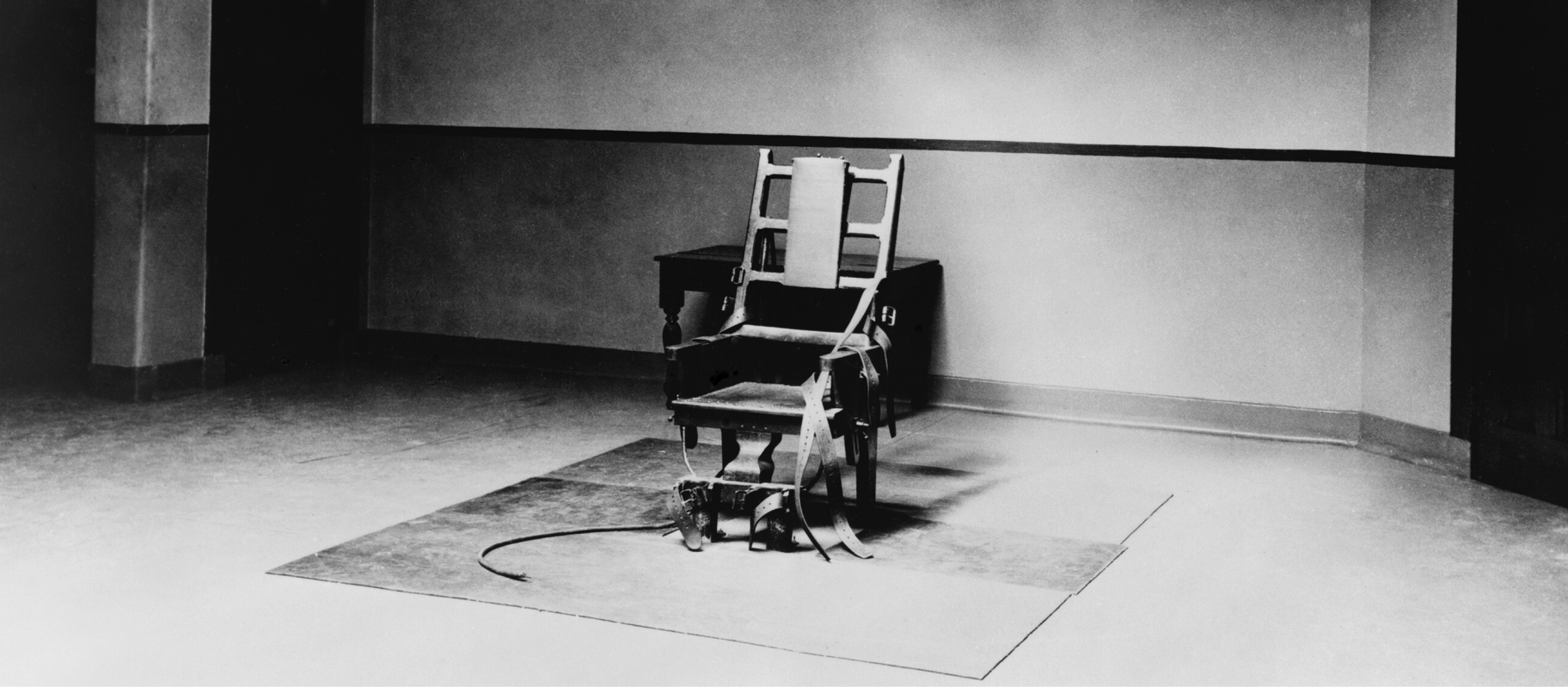 Black and white photo of an electric chair in the centre of a room.