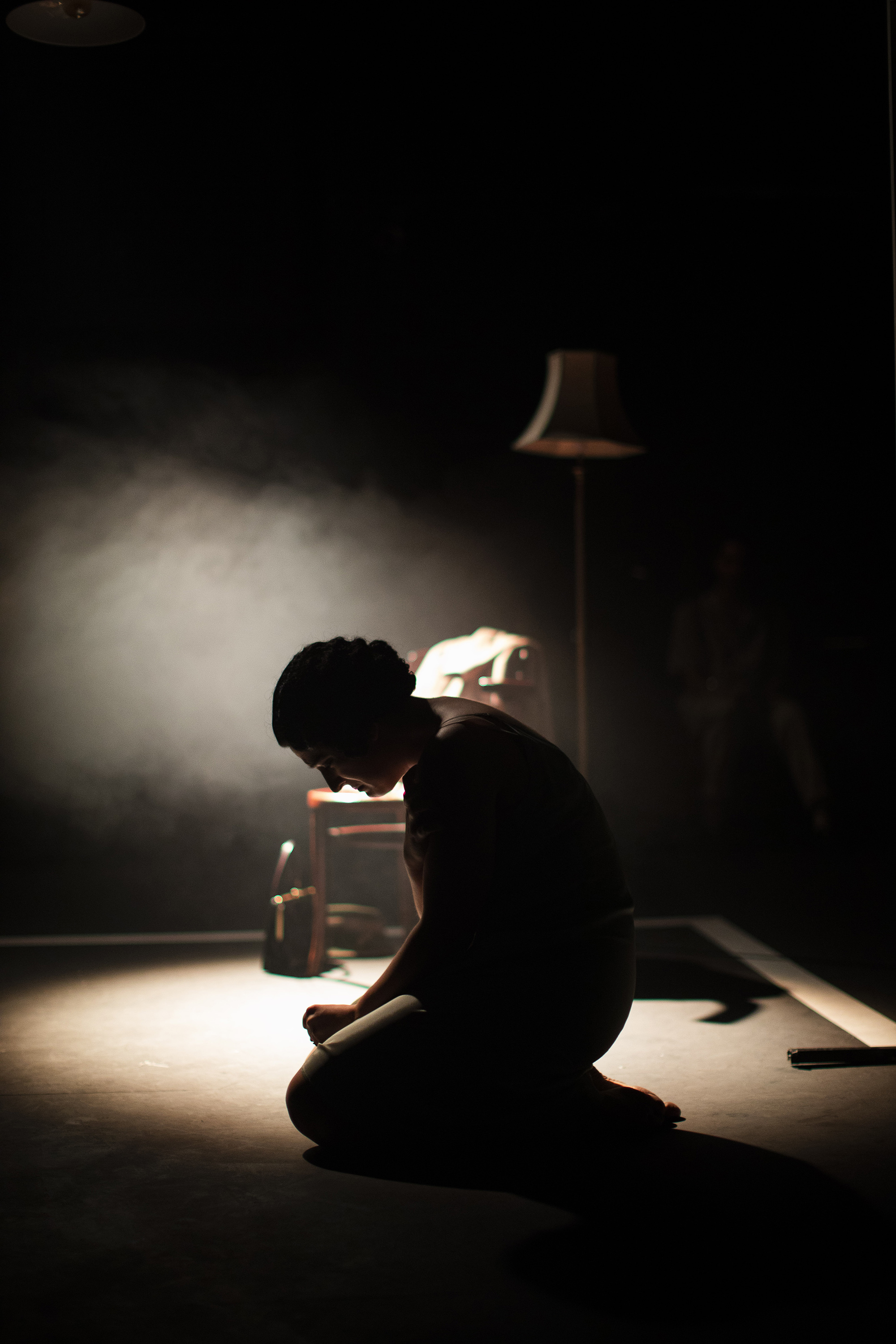 Person kneeling on the floor with a spotlight behind them.