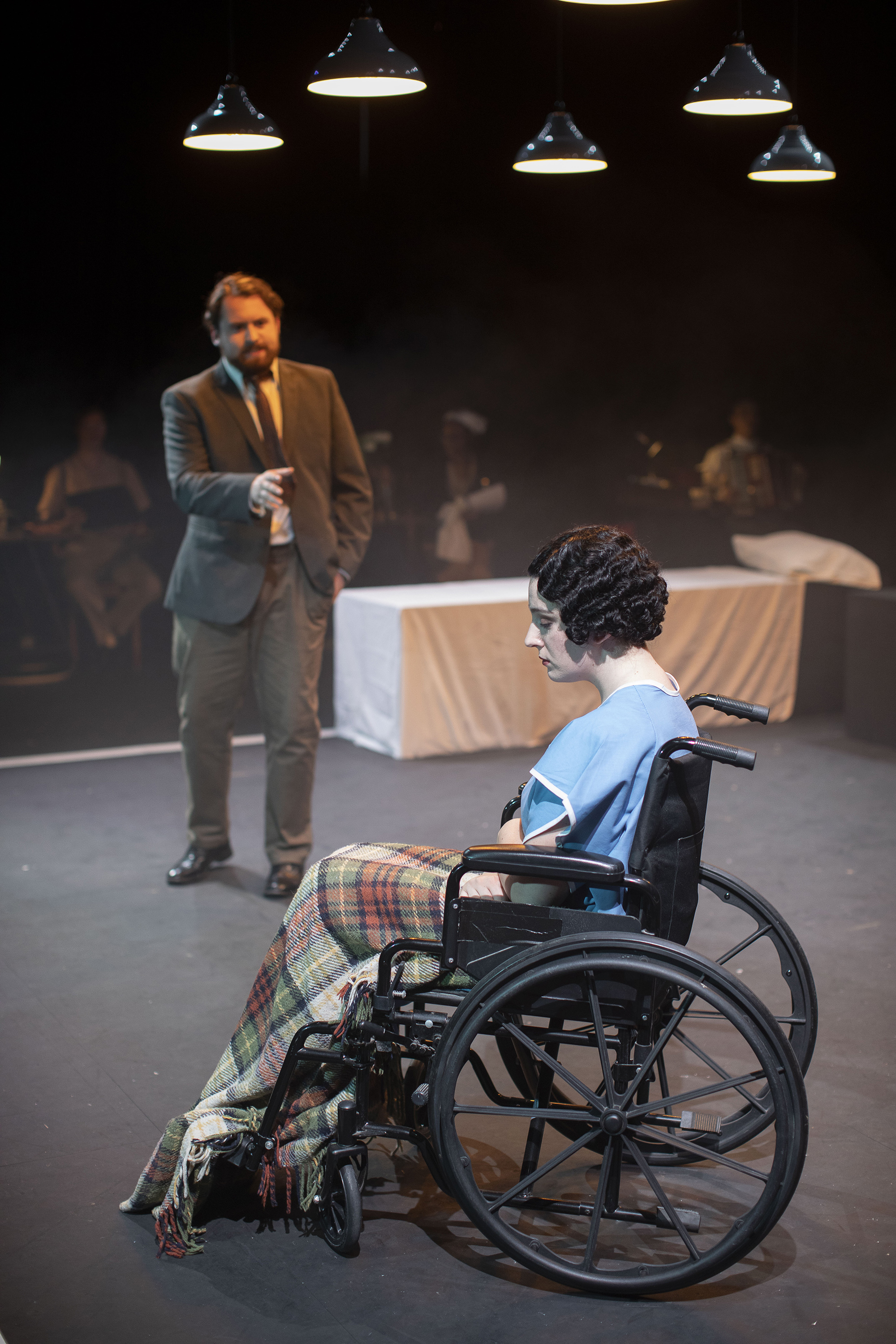 A person sitting in a wheelchair. Another person stands in front of them and gestures towards them.