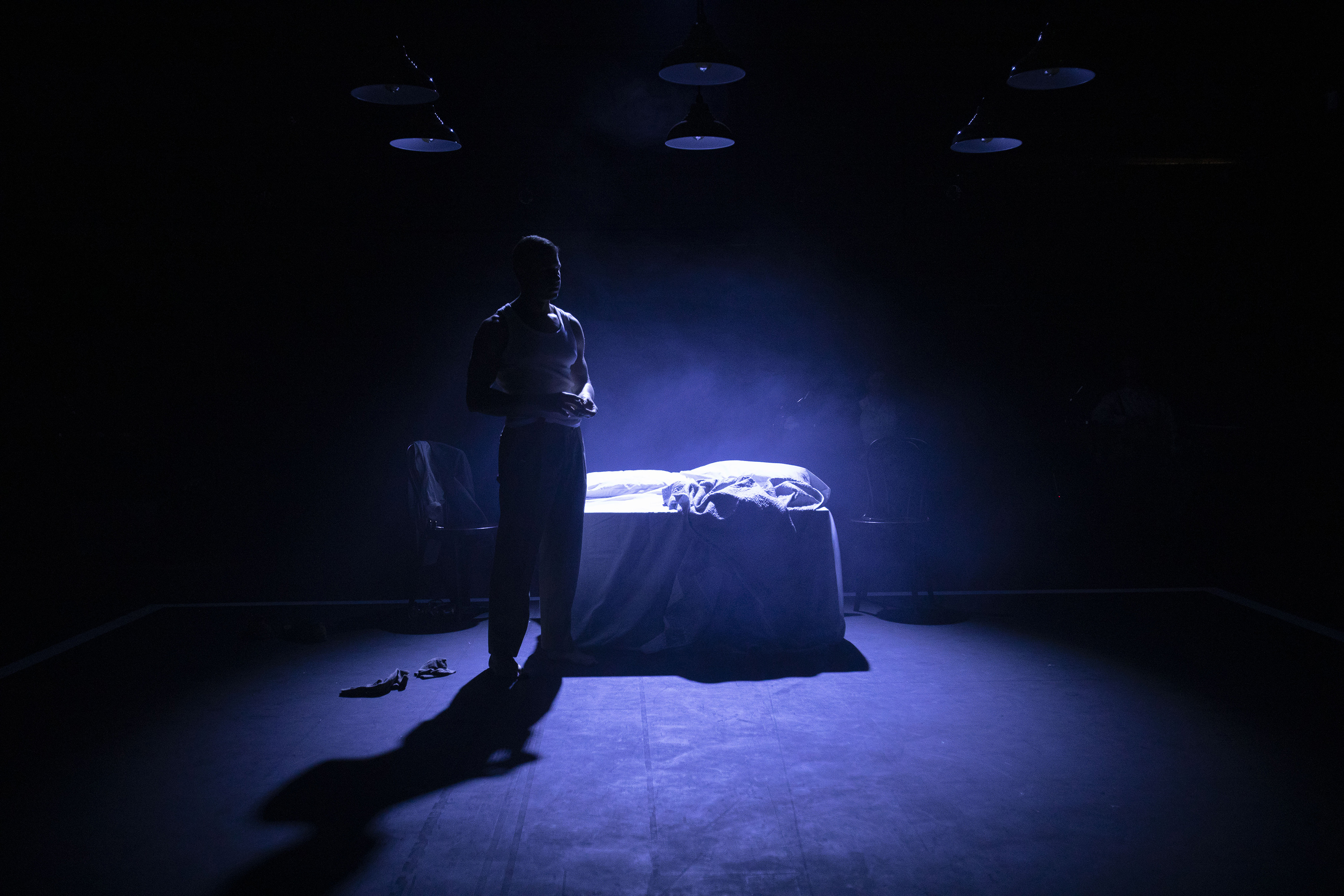 Person stands by a bed with a spotlight behind them.