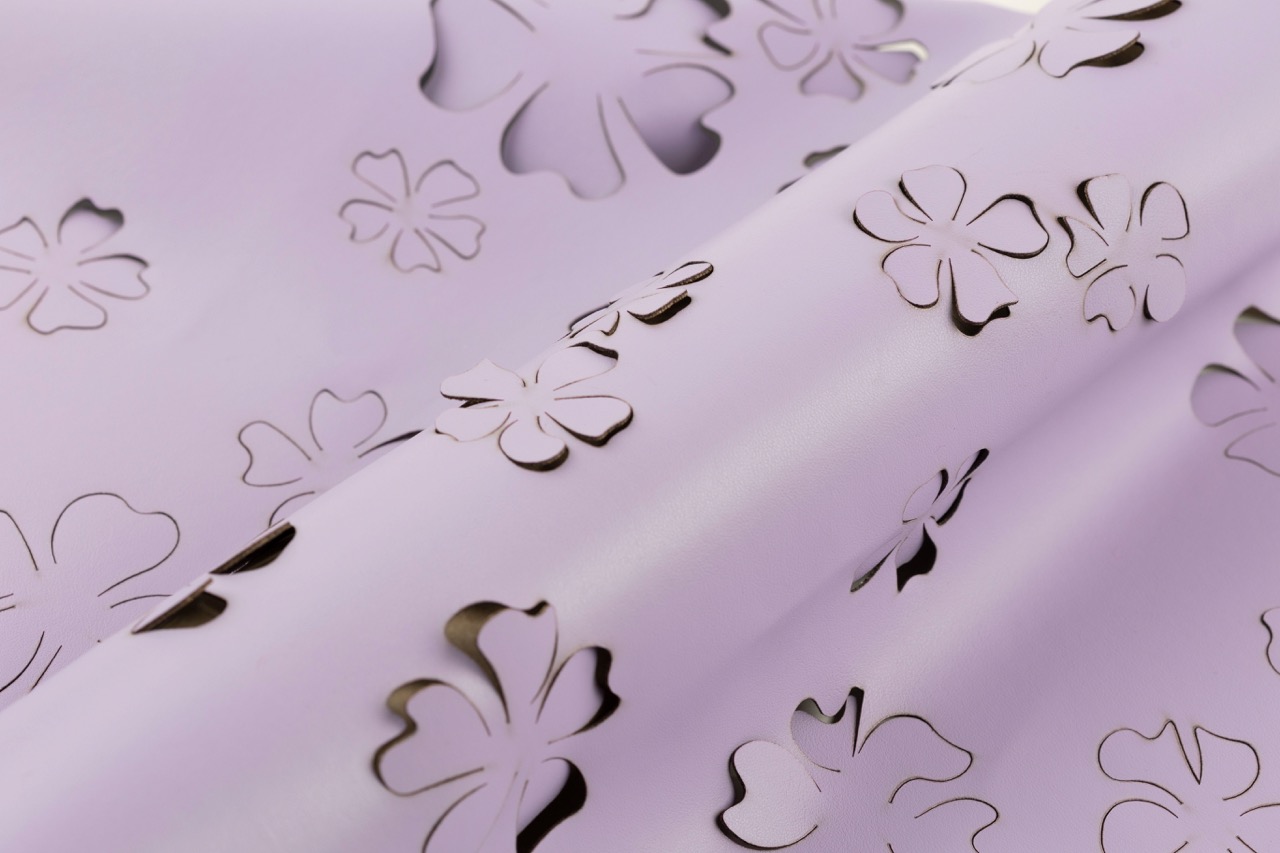 A lavender sheet of paper featuring a pattern of cut-out flowers in various sizes. The flowers expose a contrasting darker background, creating an intricate design.