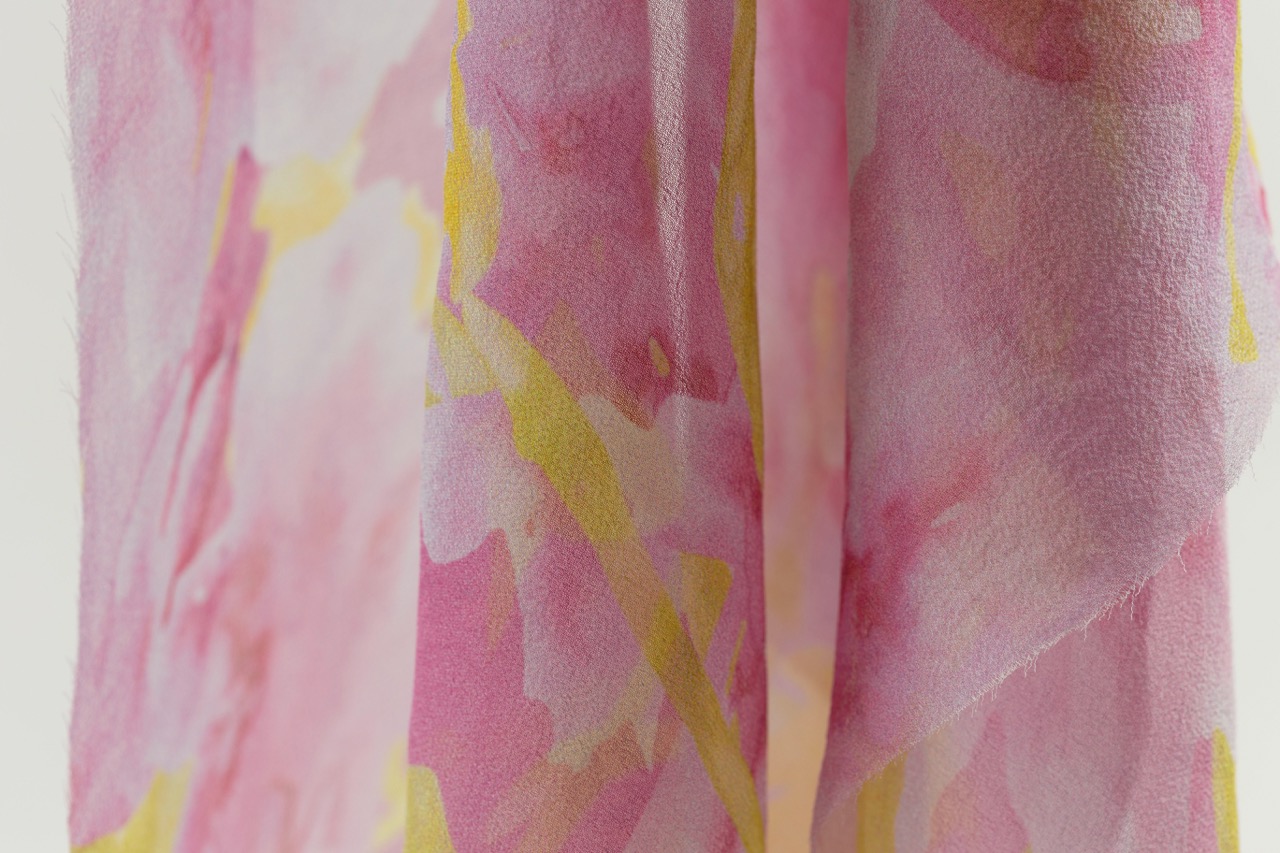 A close-up of a pink and yellow patterned fabric, featuring soft floral designs. The fabric appears lightweight and flowy, with folds that create an organic, textured look.