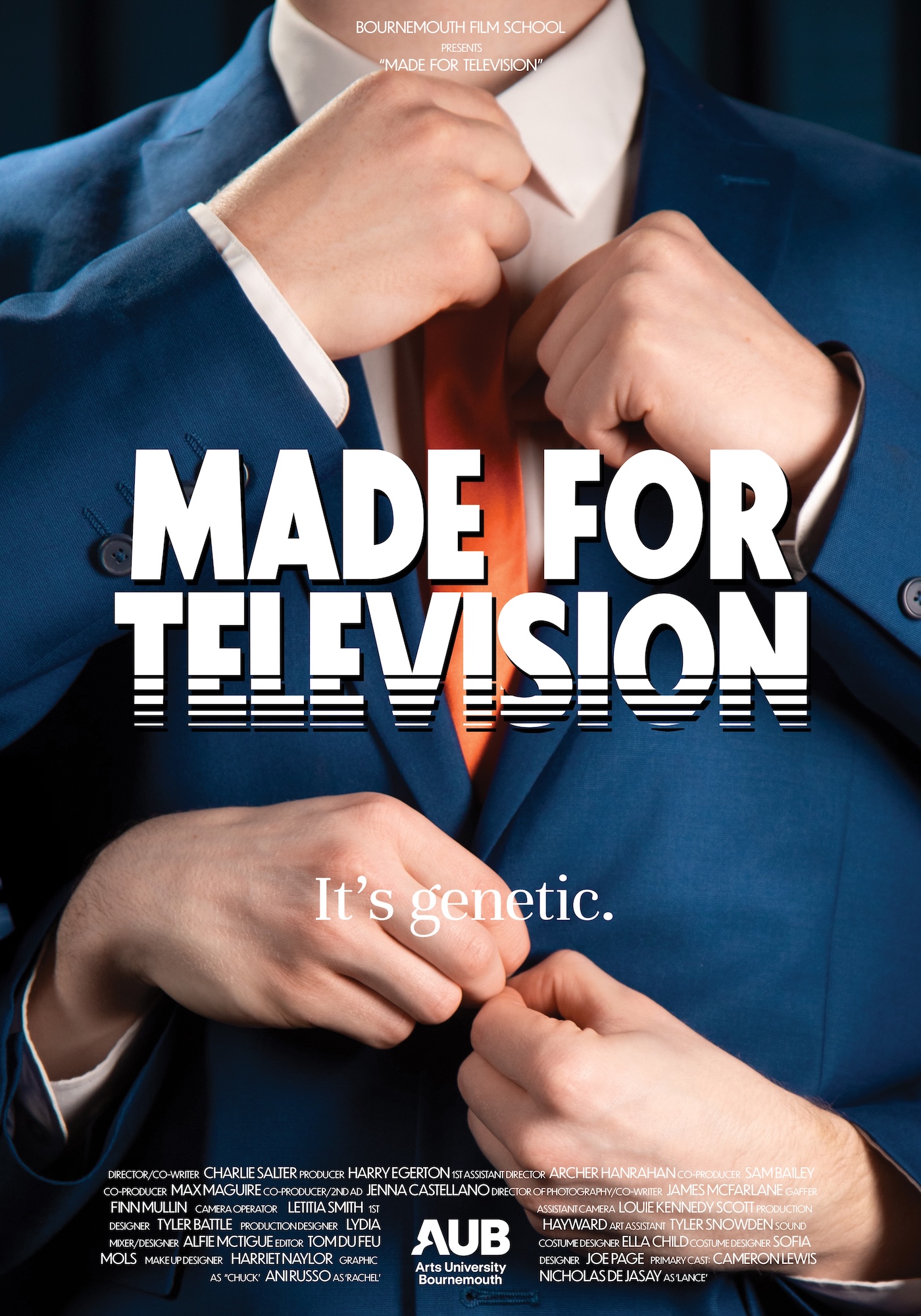 A close-up of two hands adjusting a blue suit jacket, with a vibrant orange tie visible. The background includes text that reads "MADE FOR TELEVISION" and "It's genetic." which are prominently displayed in white letters.
