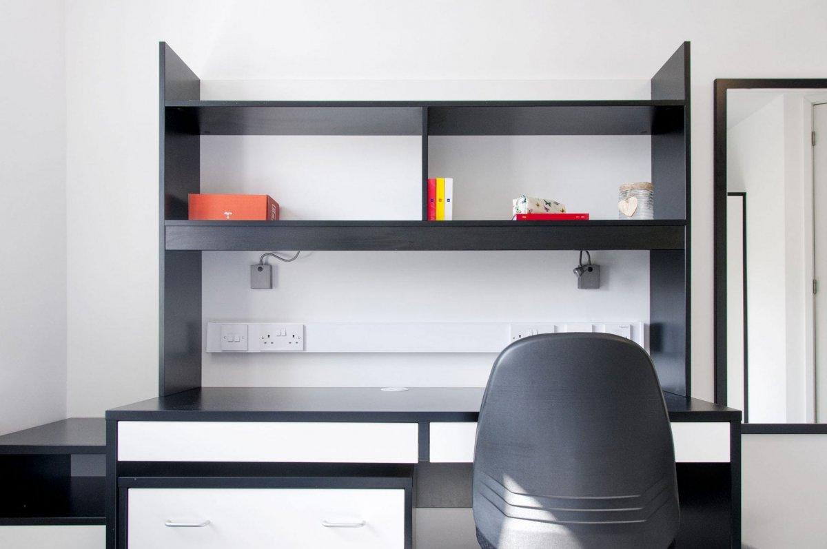 Study area within a bedroom at Madeira Road Halls, features a black desk, black shelves and shelves